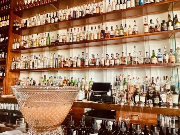 A bar with brightly lit shelves reaching to the ceiling lined with bottles.