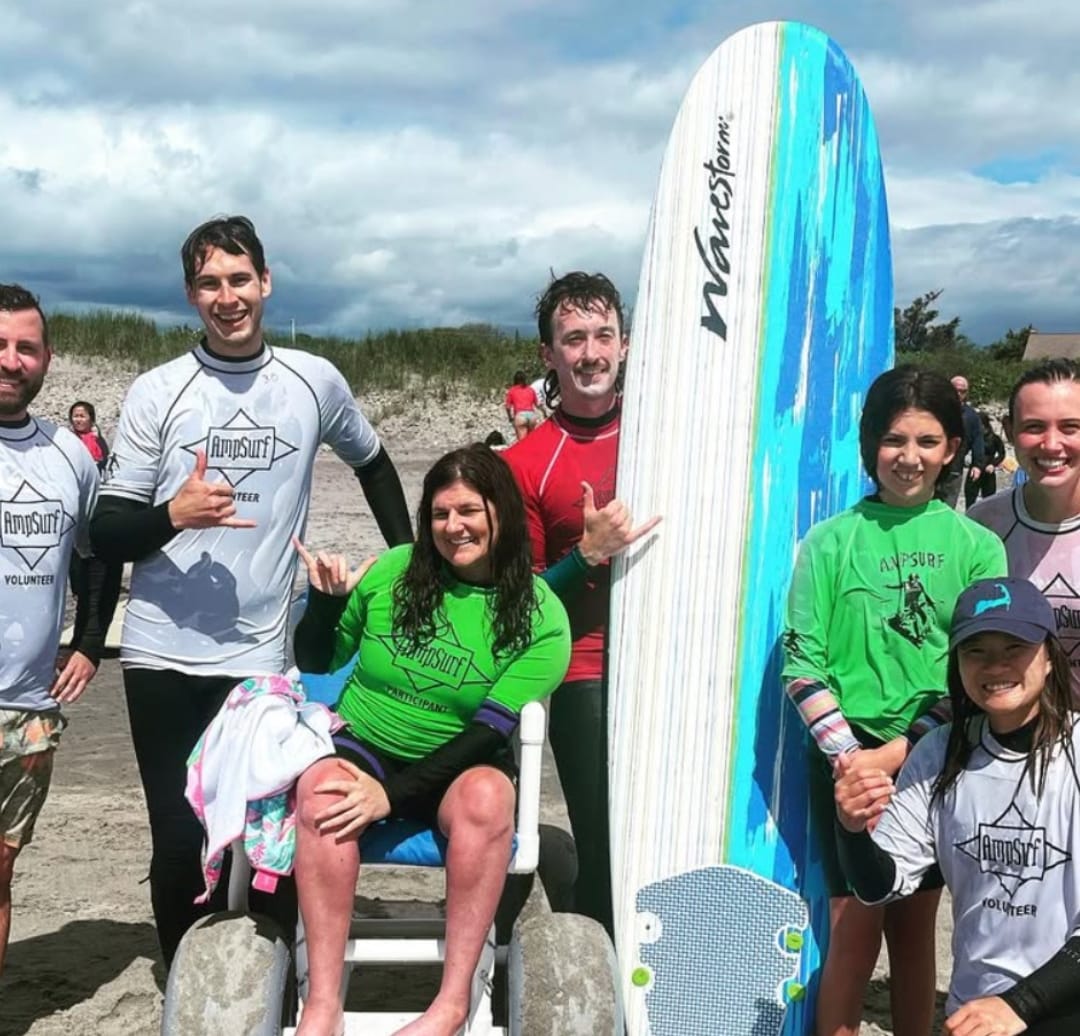 a group of people smile on a beach near a surfboard