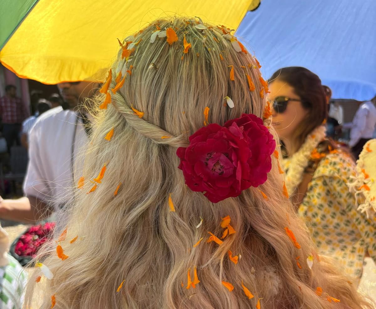 a red rose and orange flower petals decorate a woman's long blonde hair