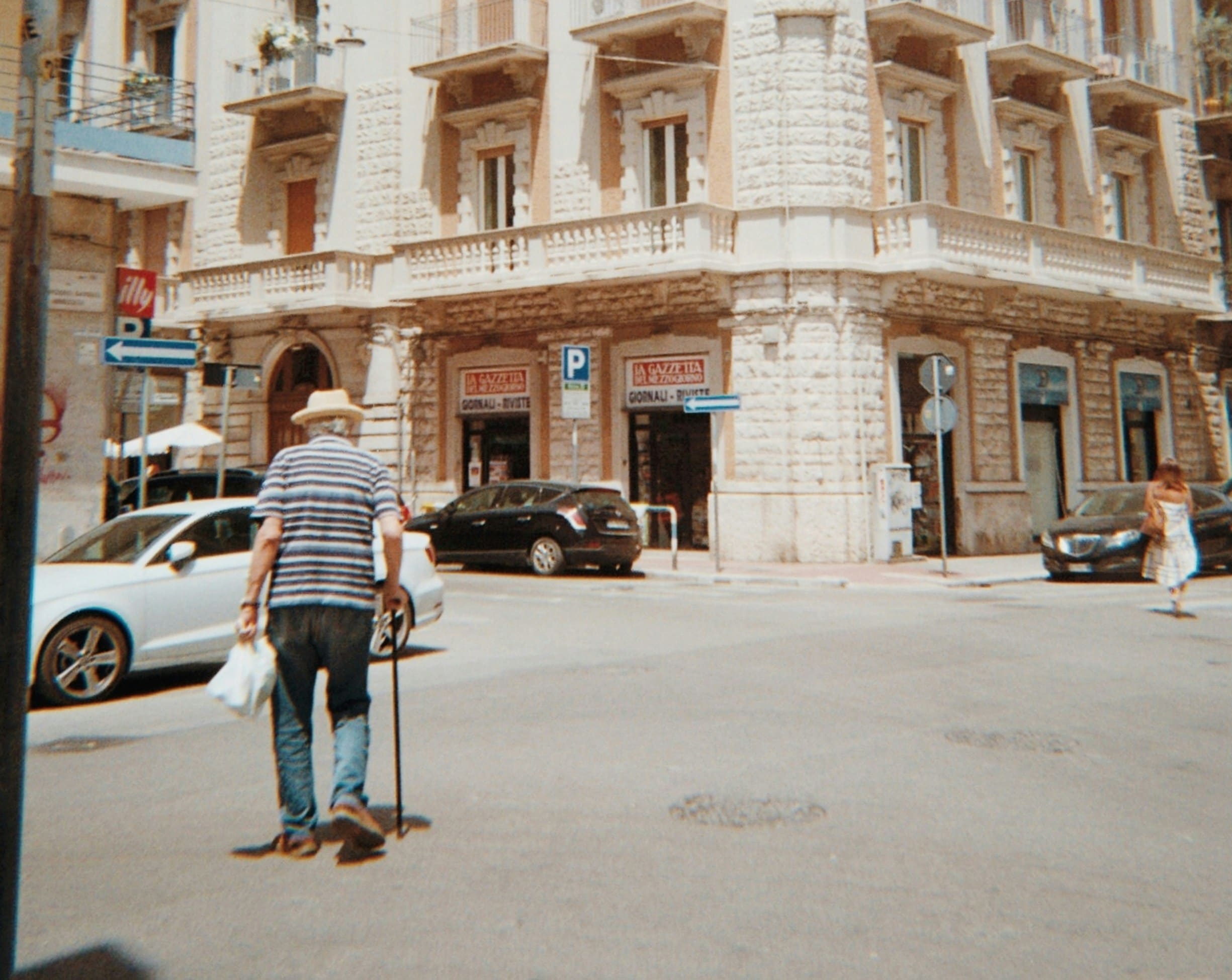 a man with a cane walks in the street on a sunny day