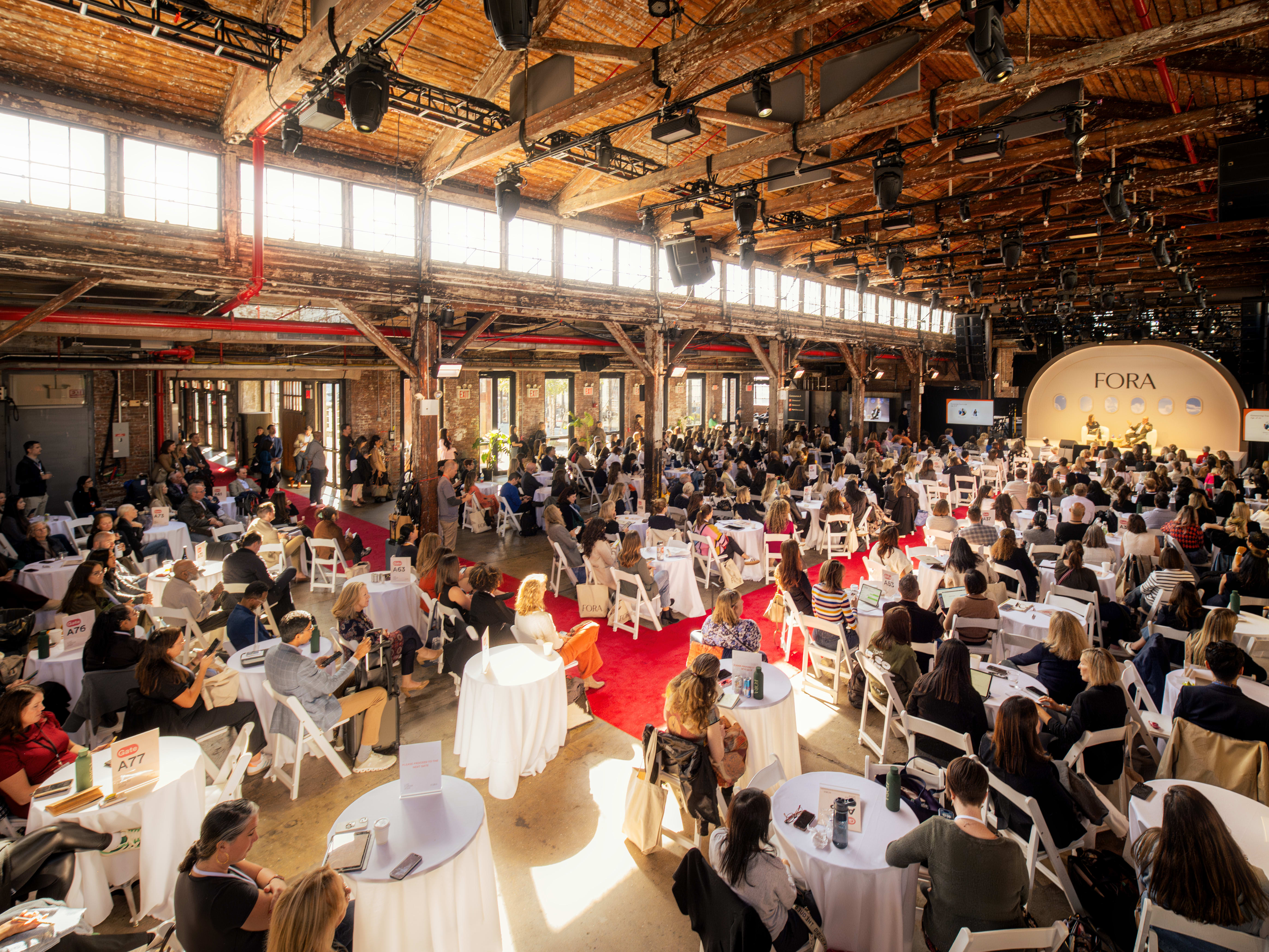 seated audience in a large warehouse space looking at a stage
