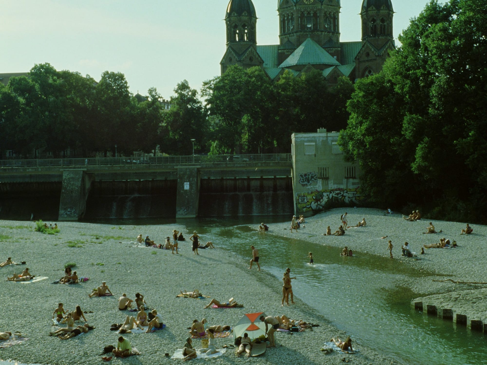 A group of people laying on top of a sandy beach at Isar in Munich.
