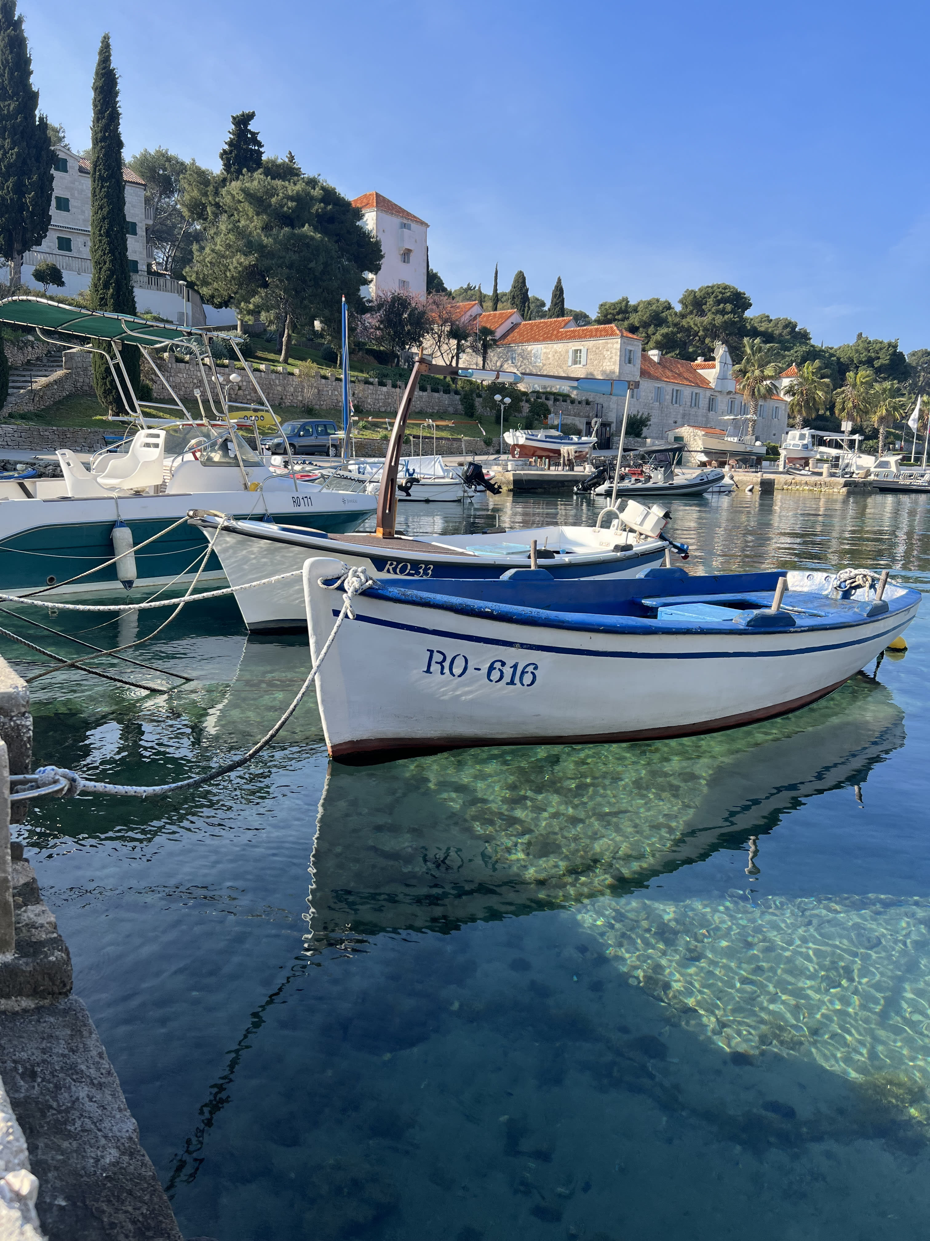 Smaller fisher boats tied up at a pier and floating on top of crystal clear, blue water.