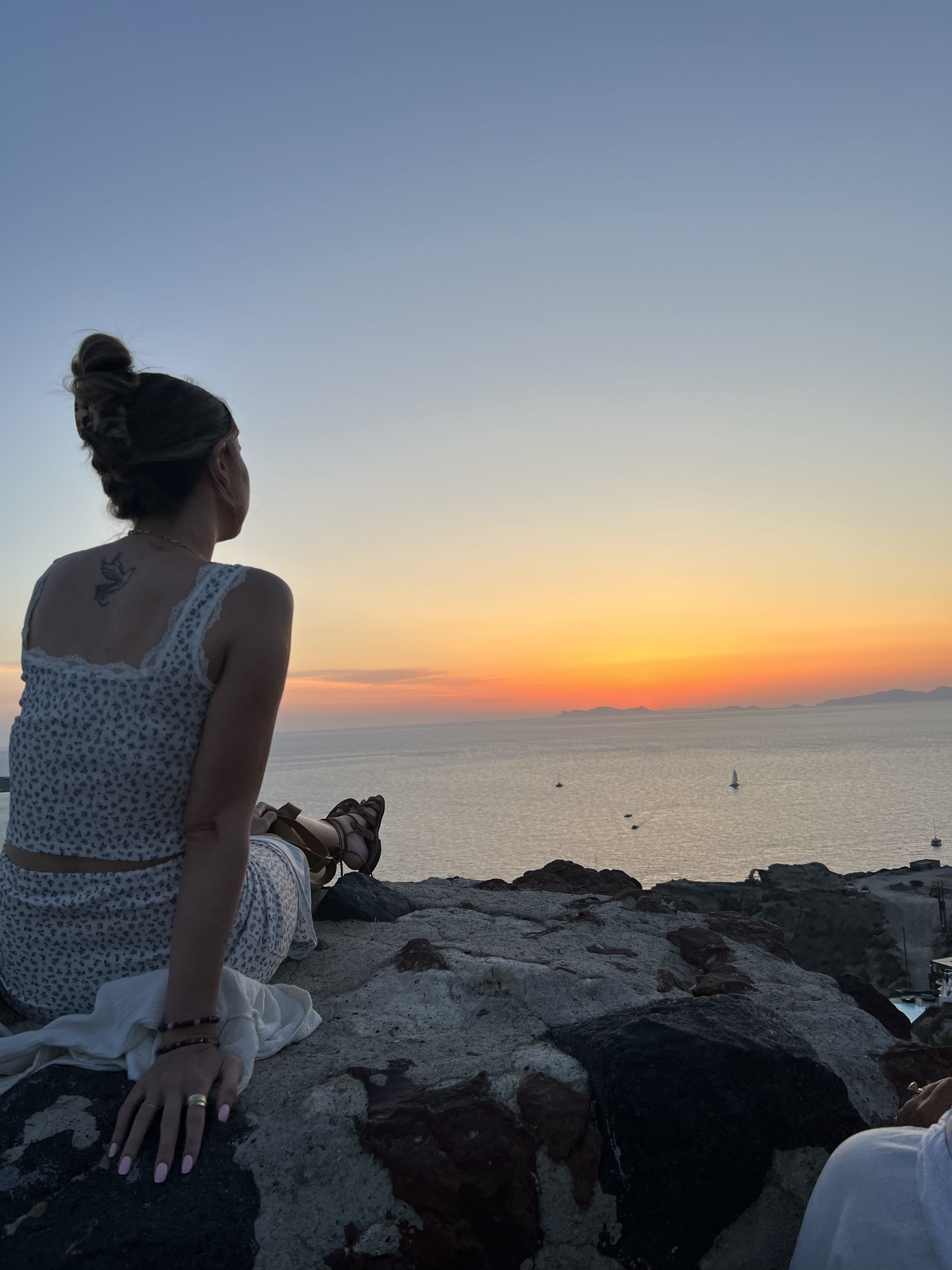 A woman sitting on rocks watching the sunset over the ocean.