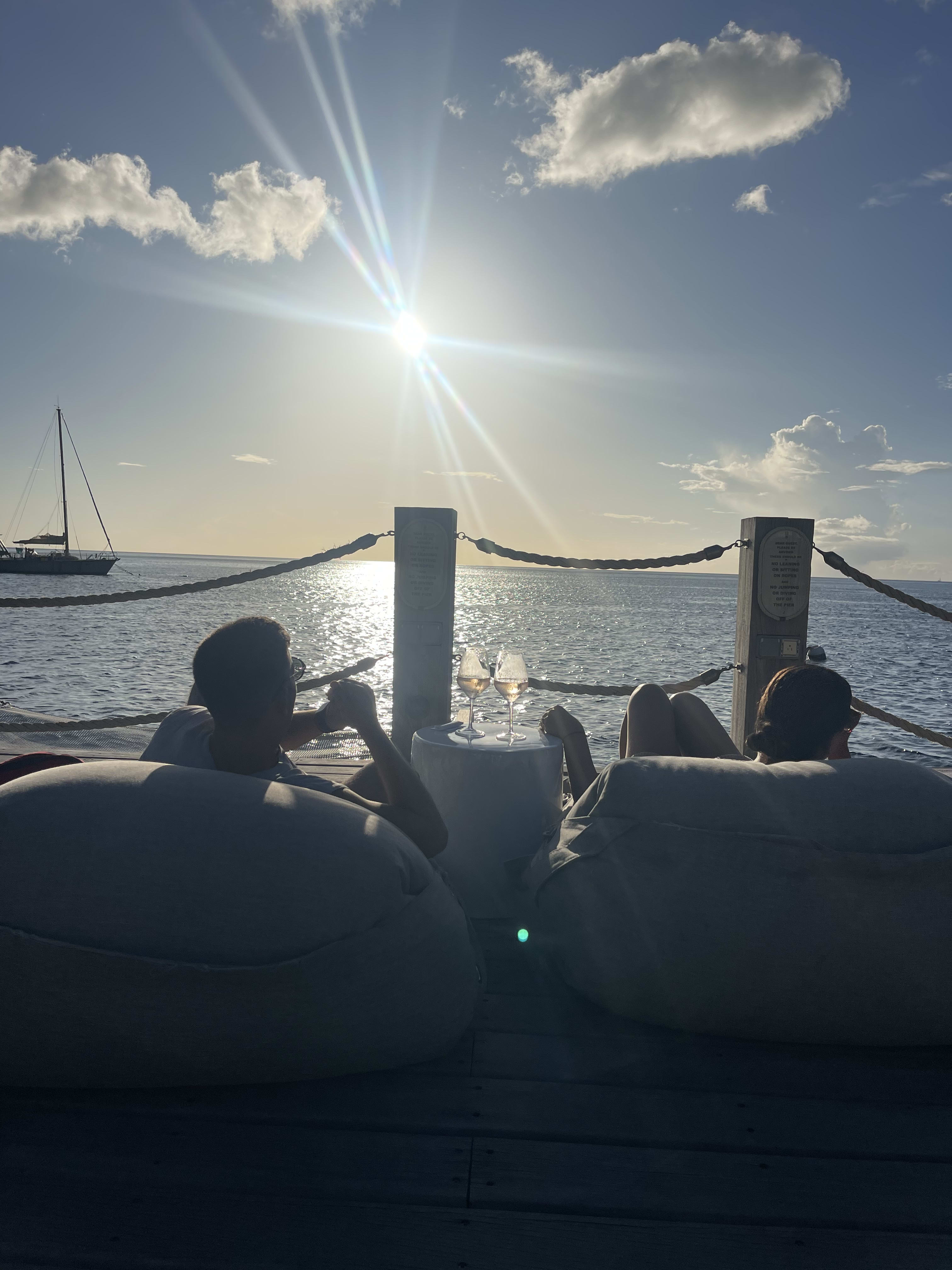 A man and a woman drinking wine and lounging on a deck with drinks overlooking the sea