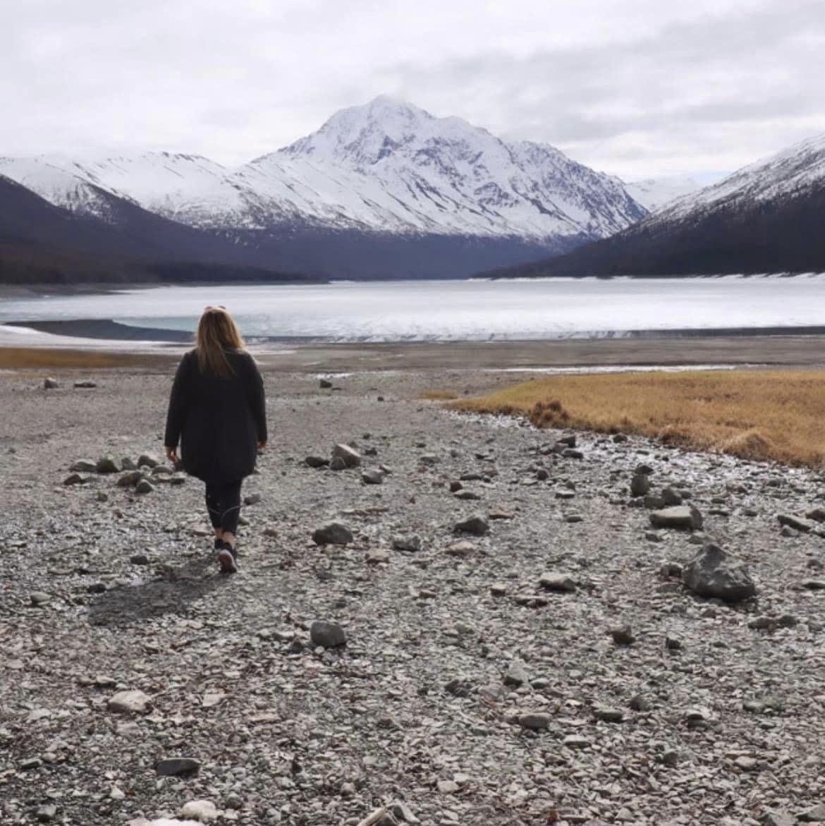 Leah with her back to the camera looking at the view of frozen lake and snow capped mountains.