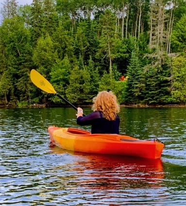 Picture of Paige kayaking in a river with foliage in the distance