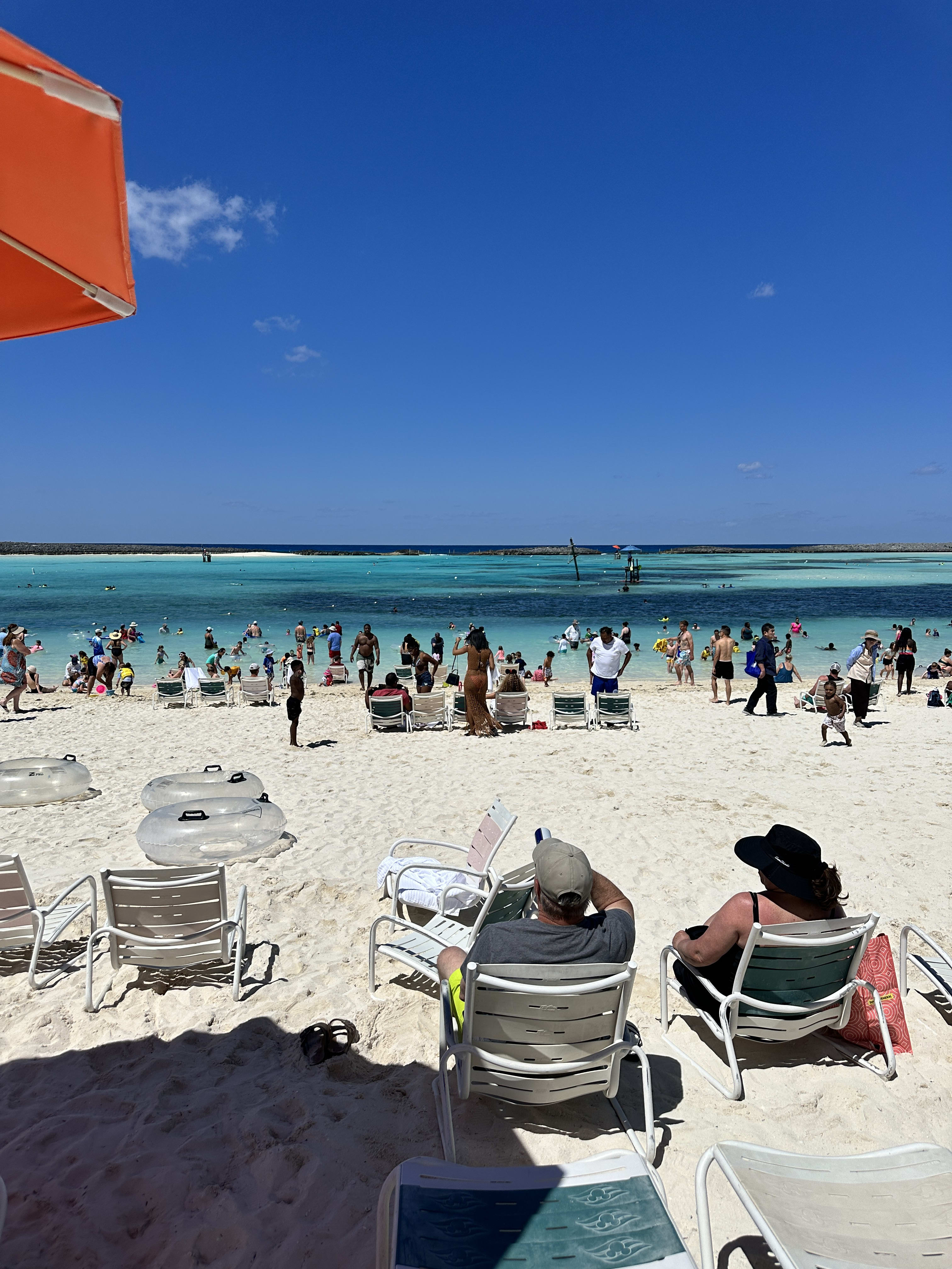 A crowded white sand beach with crystal clear blue water at it's shore.