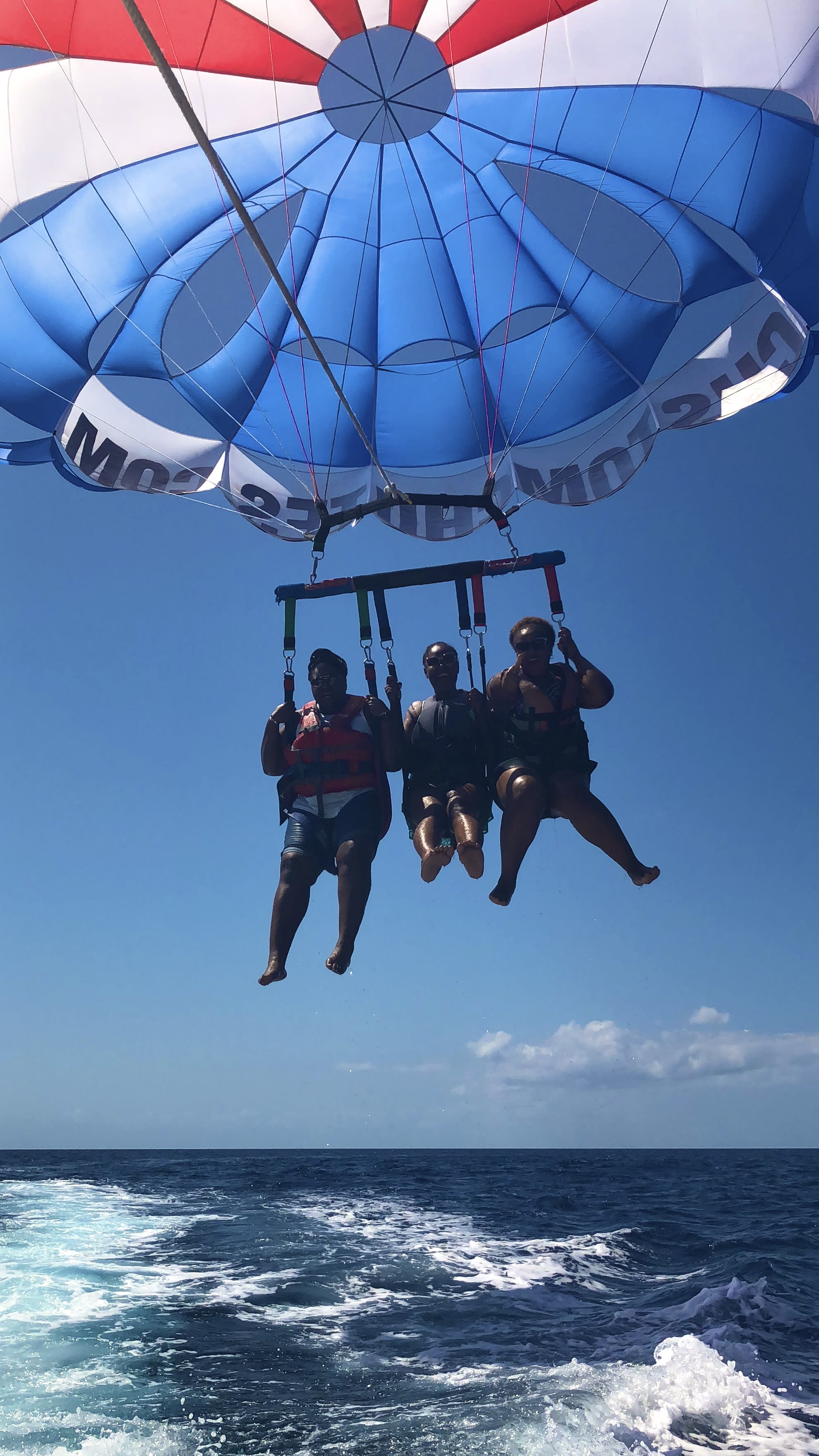 A photo of three people descending from a blue sky while parasailing.