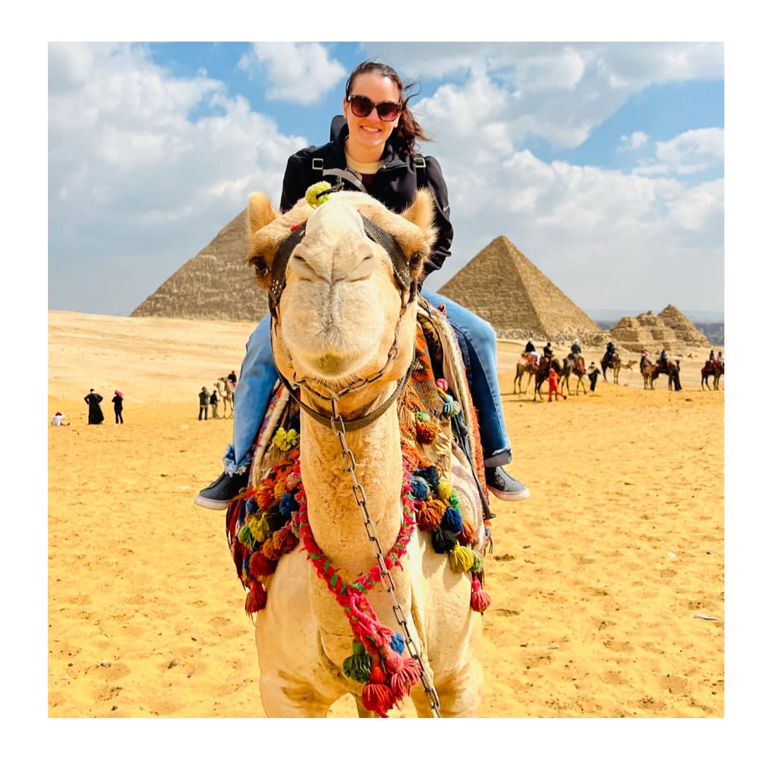 Britnee sitting on a camel in the desert with pyramids in the background