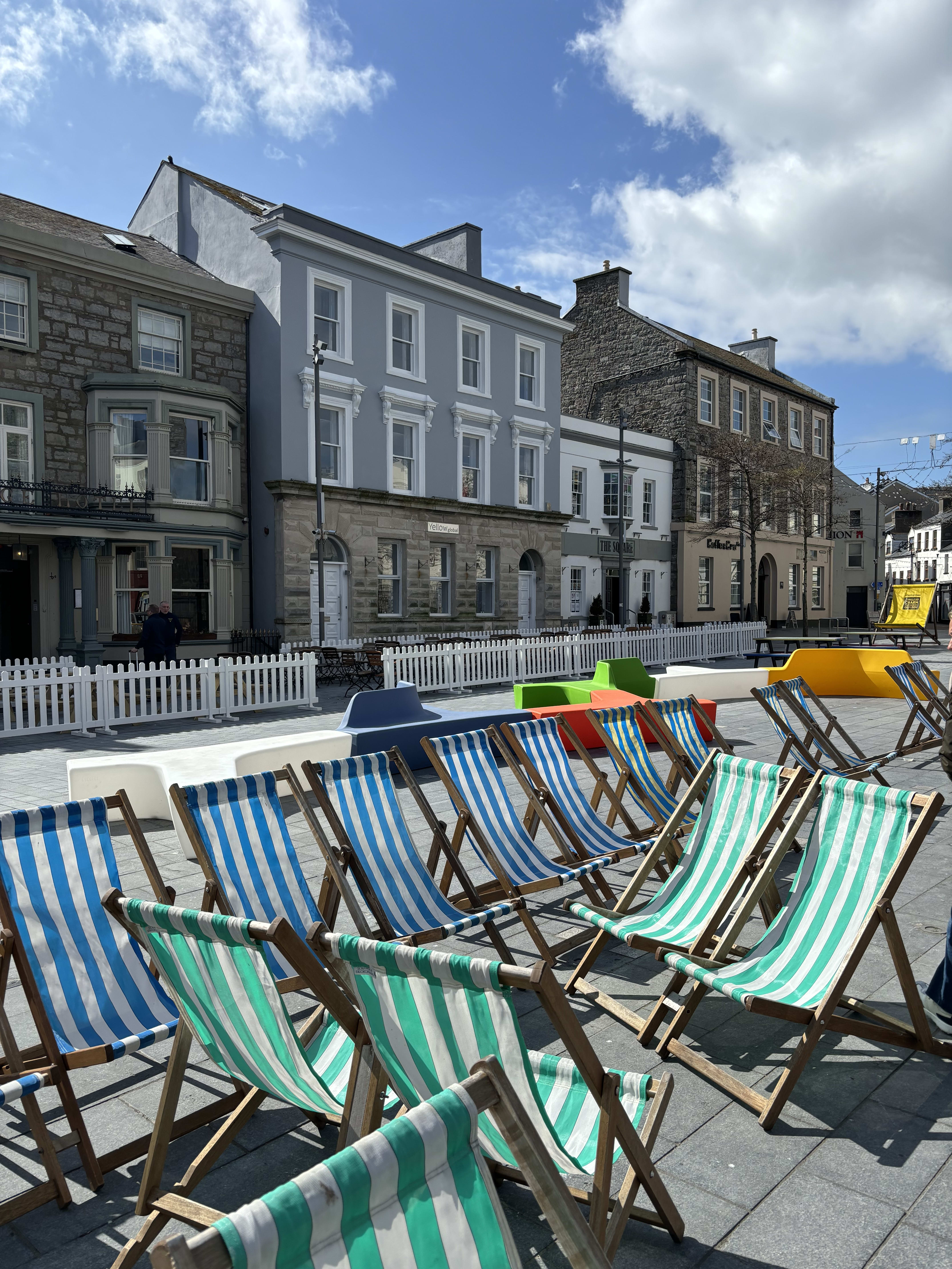 Blue, green, and white striped chairs on the side of a street with small buildings in the background