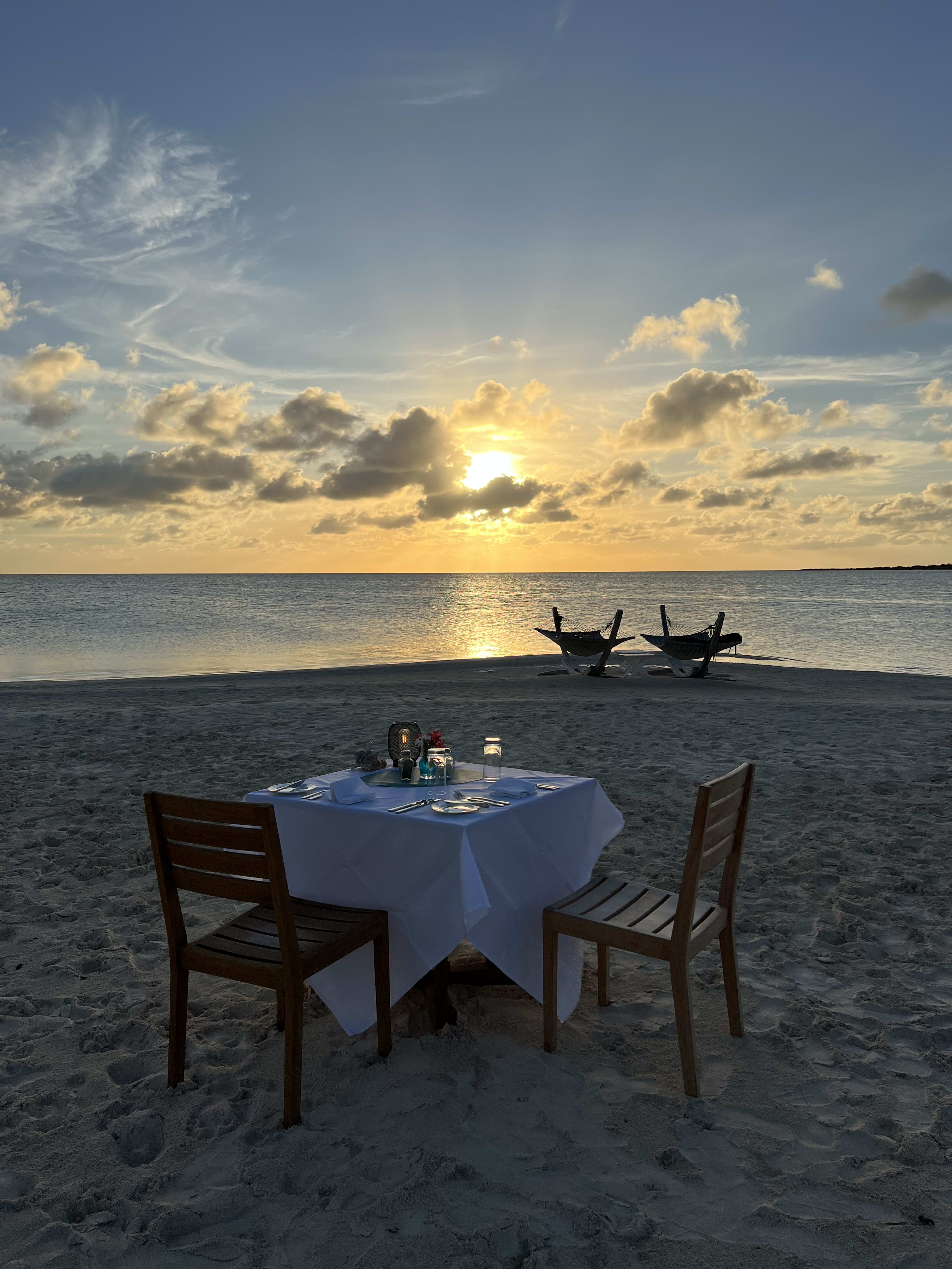 Two empty chairs and a dinner table on the beach at sunset