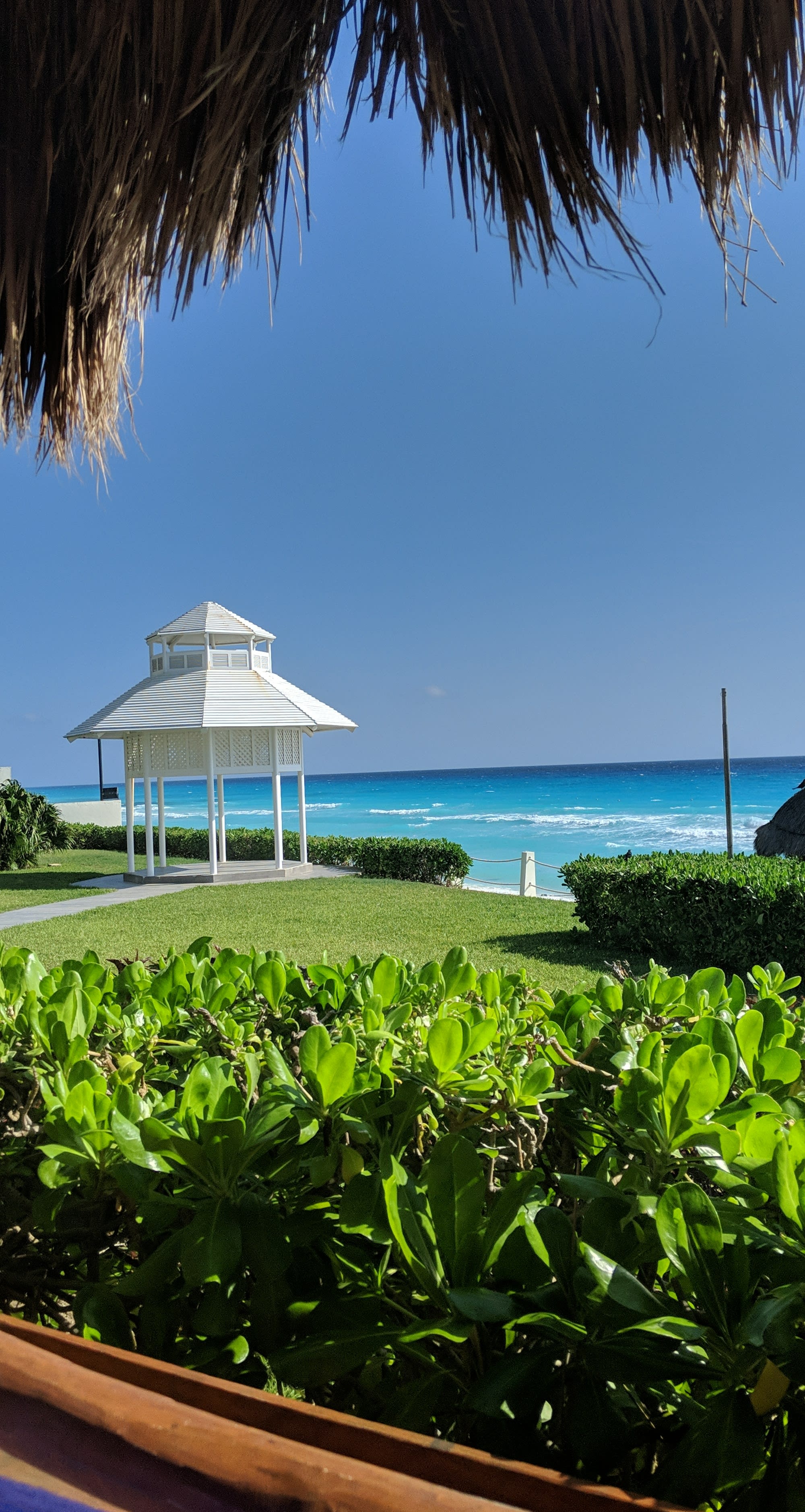 Beautiful view of a green lawn with a white gazebo stretching to the beach