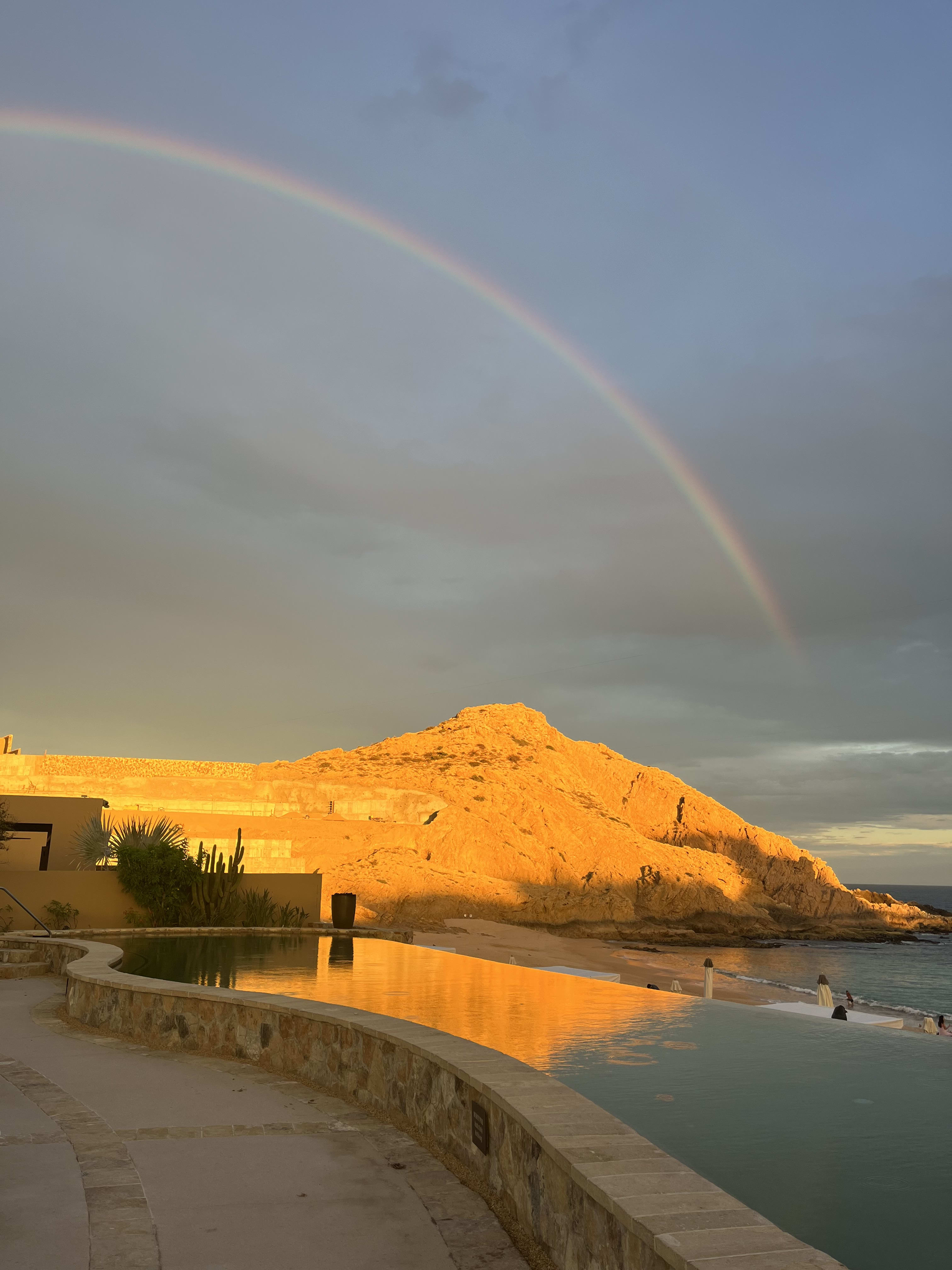 Beautiful view of rainbow stretching over a mountain alongside the sea