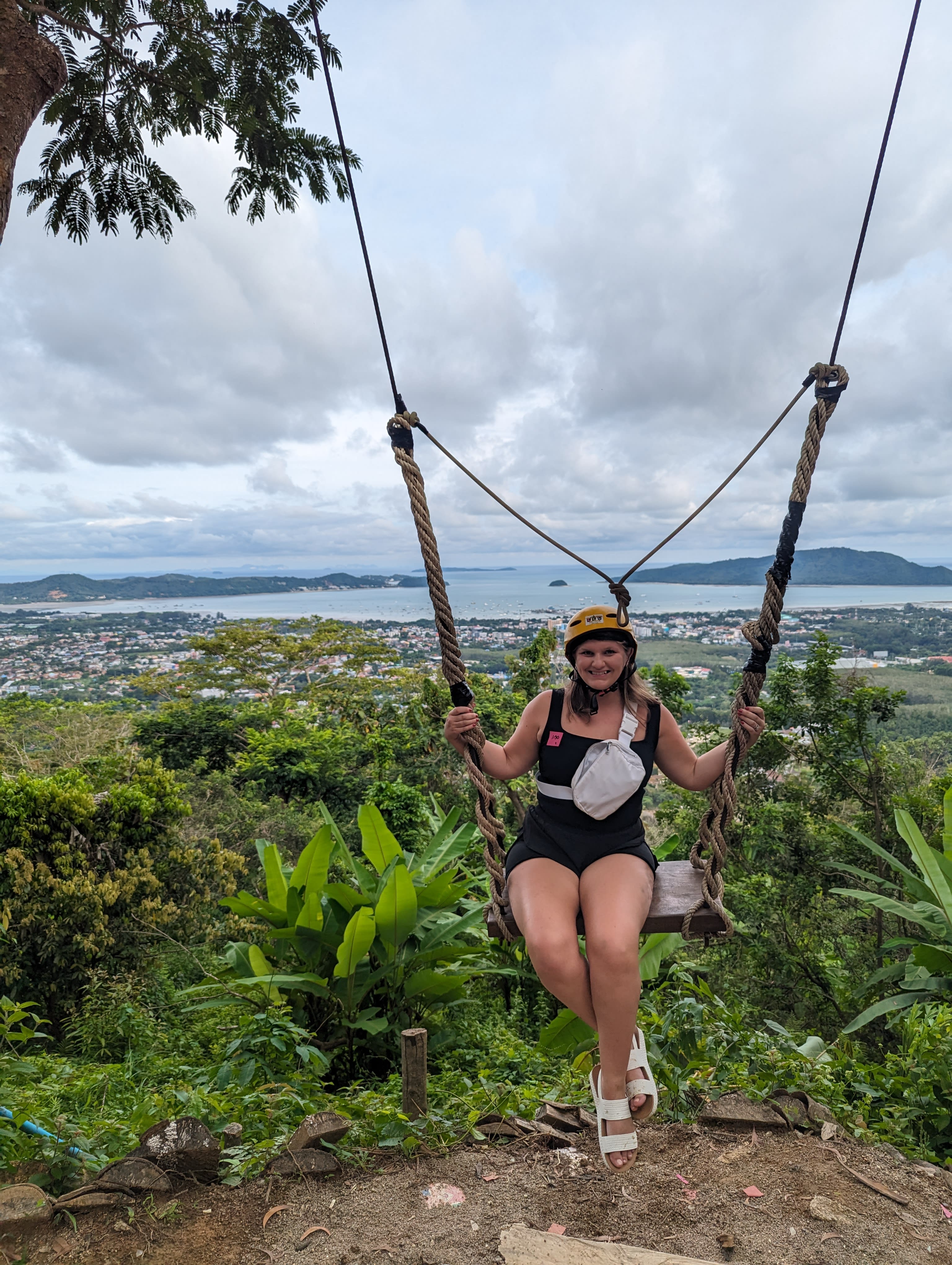 Picture of Rachel wearing a helmet on swing in the jungle with ocean views in the distance