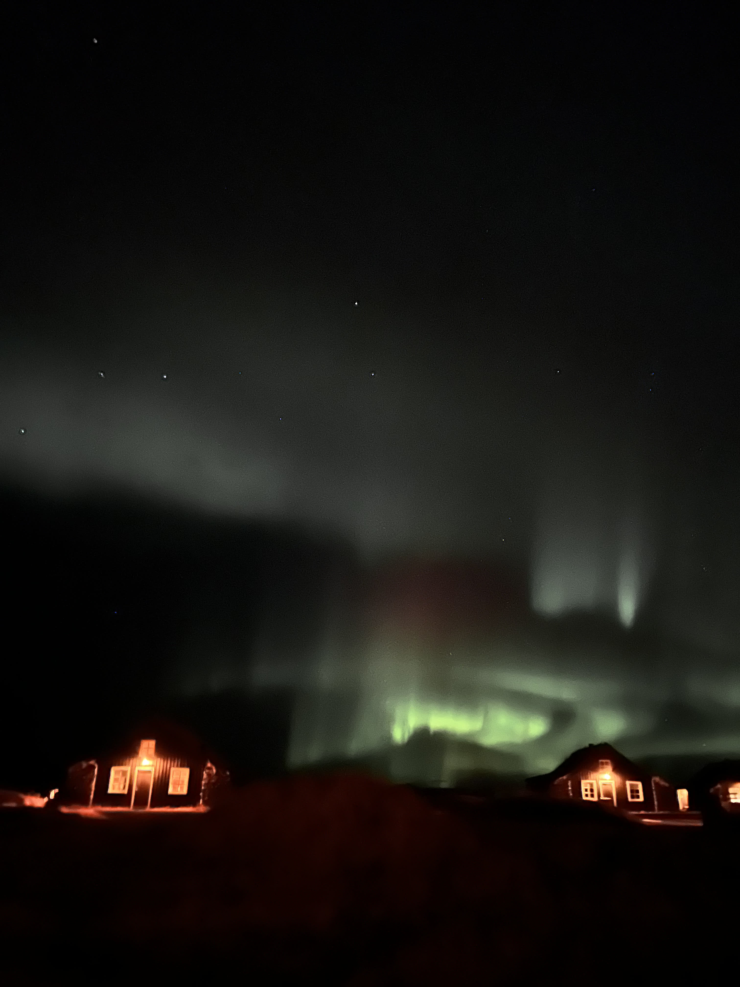 View of the Northern lights and houses lit up at night against the black sky
