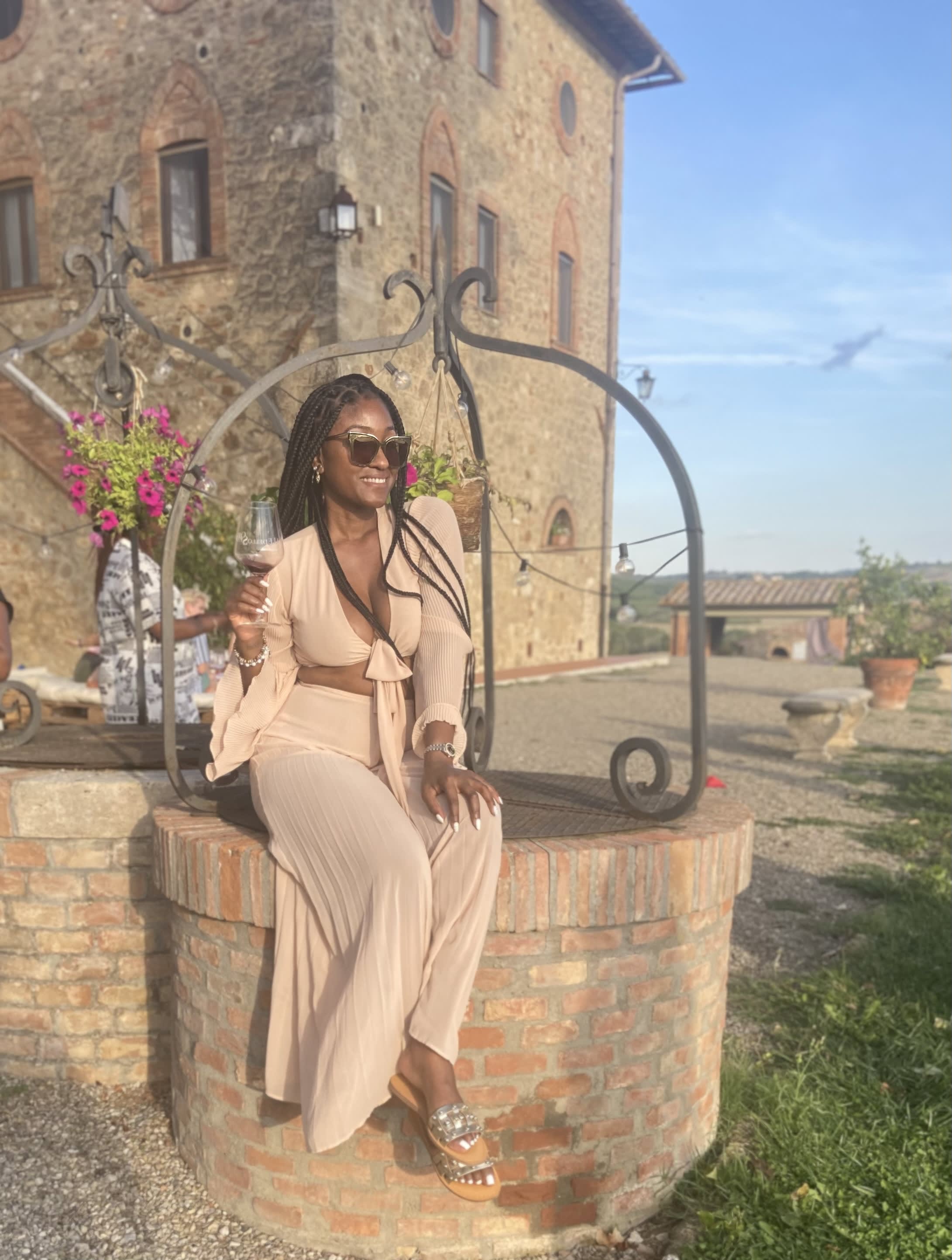 Chardon sitting outside of an old, stone mansion holding a glass of wine.