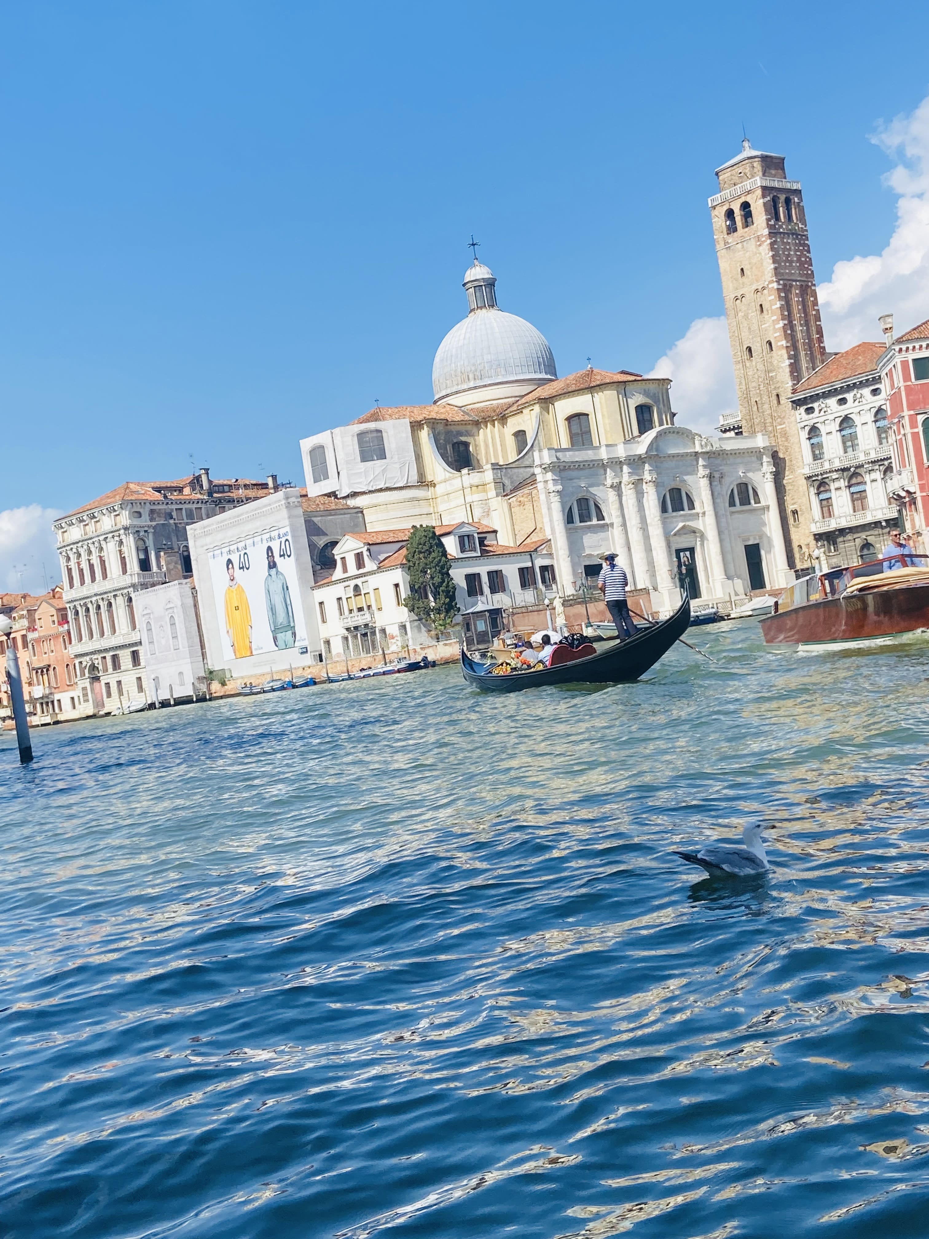 A photo of a Venetian-style boat floating in a clear blue river in front of a palace.