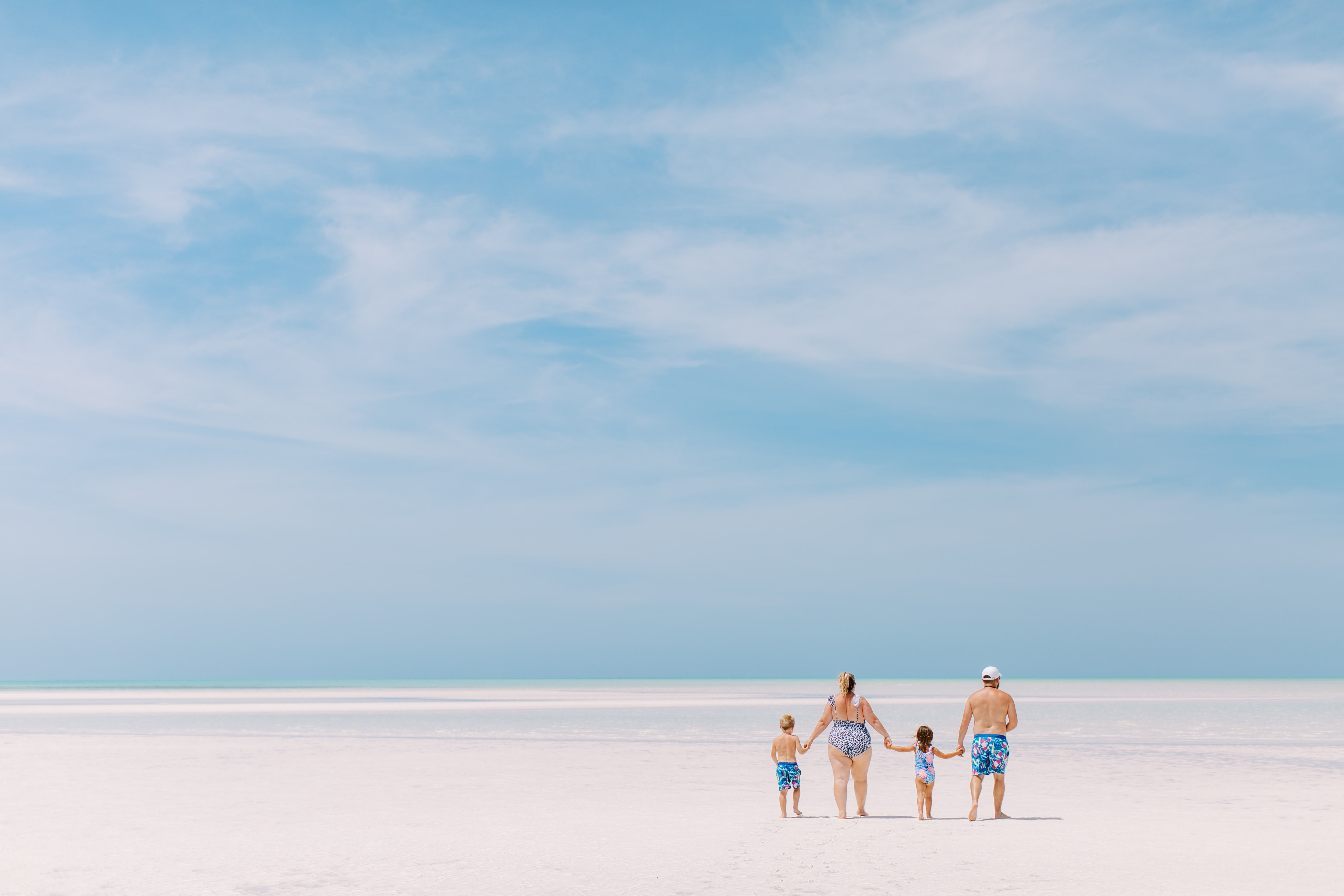 A photo of a family on an empty, white sand beach on a slightly cloudy day.