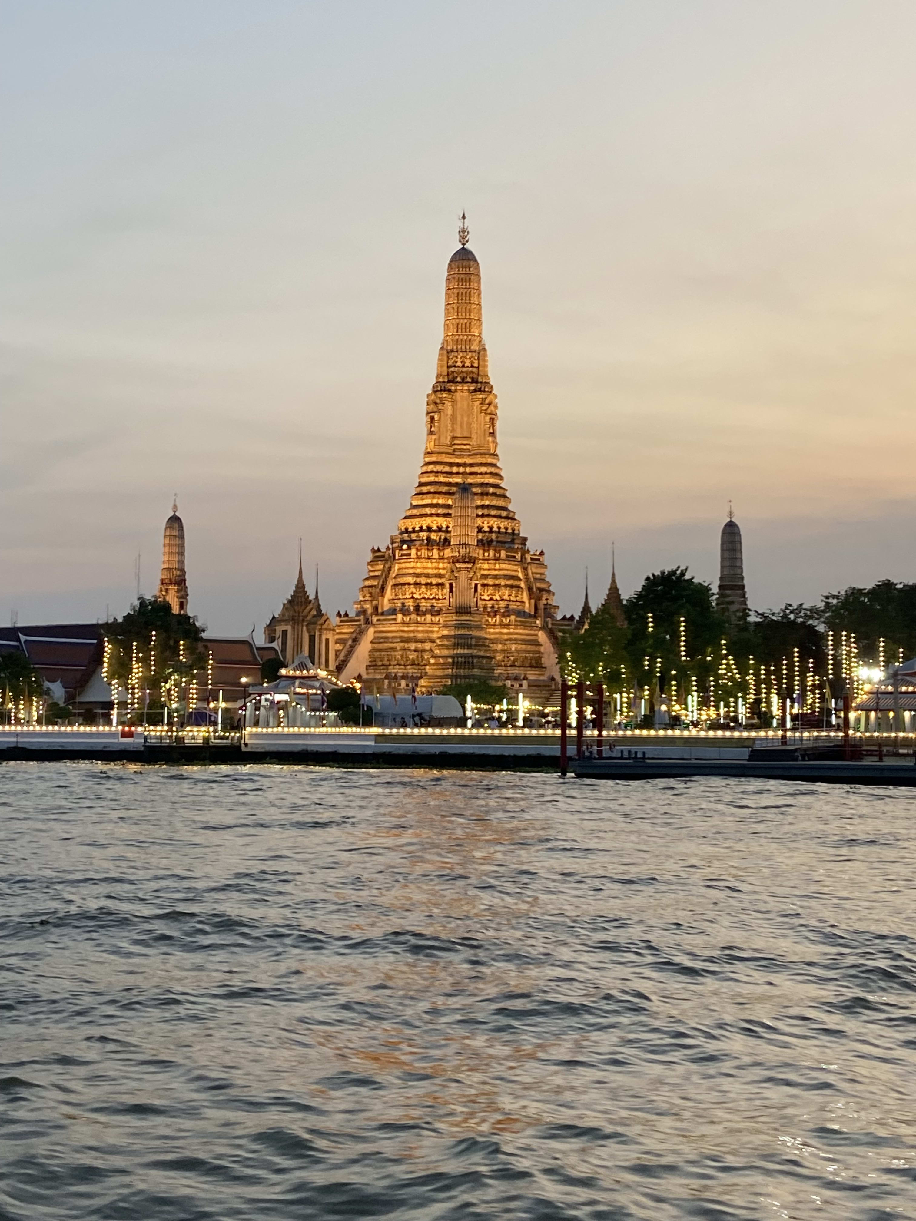 View of Wat Arun Ratchawararam Ratchawaramahawihan temple on the water lit up at sunset