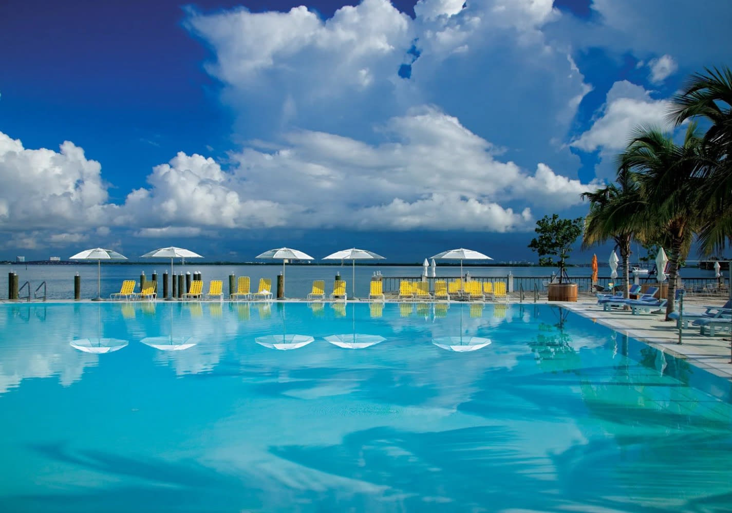 turquoise pool with white umbrellas and the ocean beyond