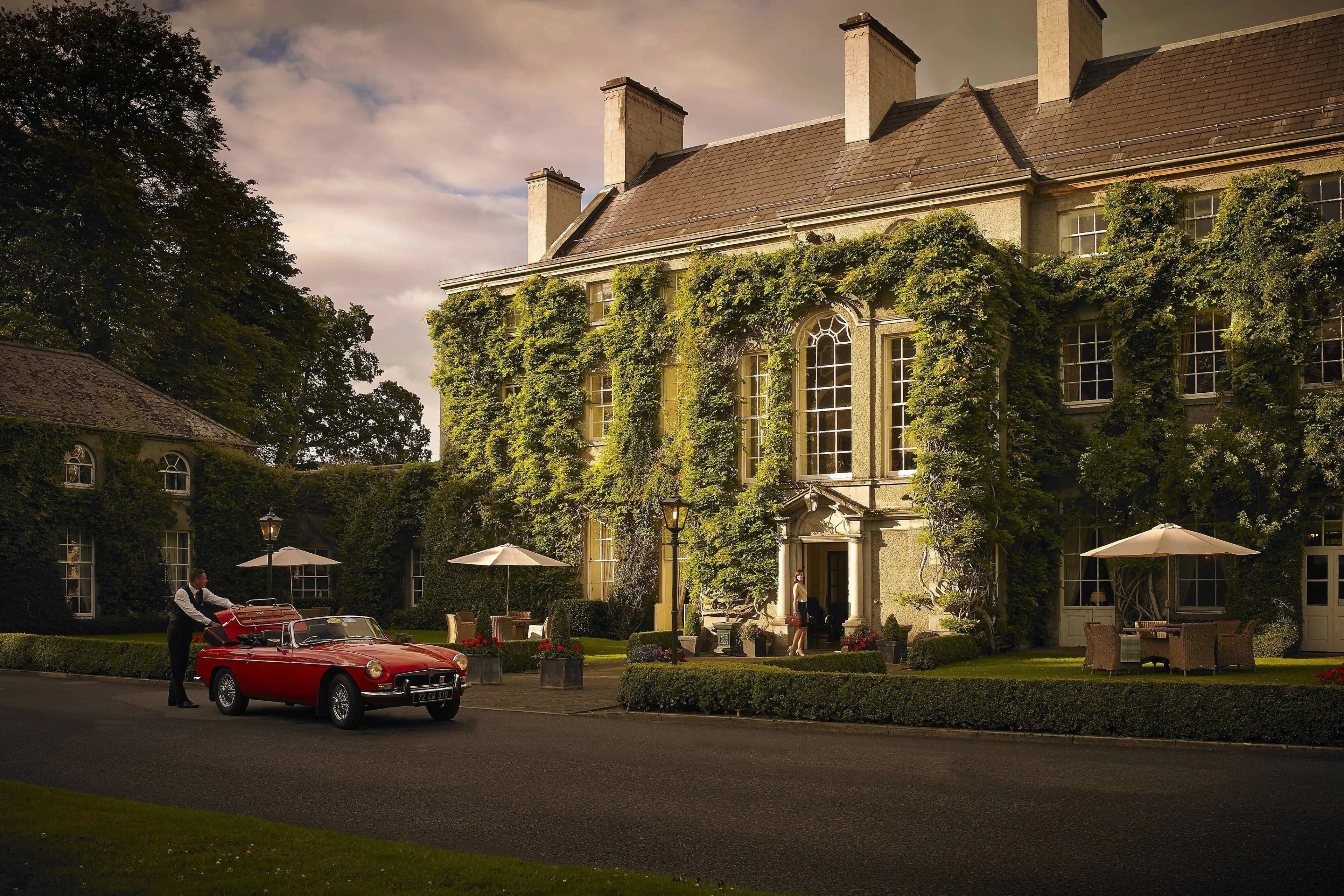 a red car in front of a manor covered in ivy