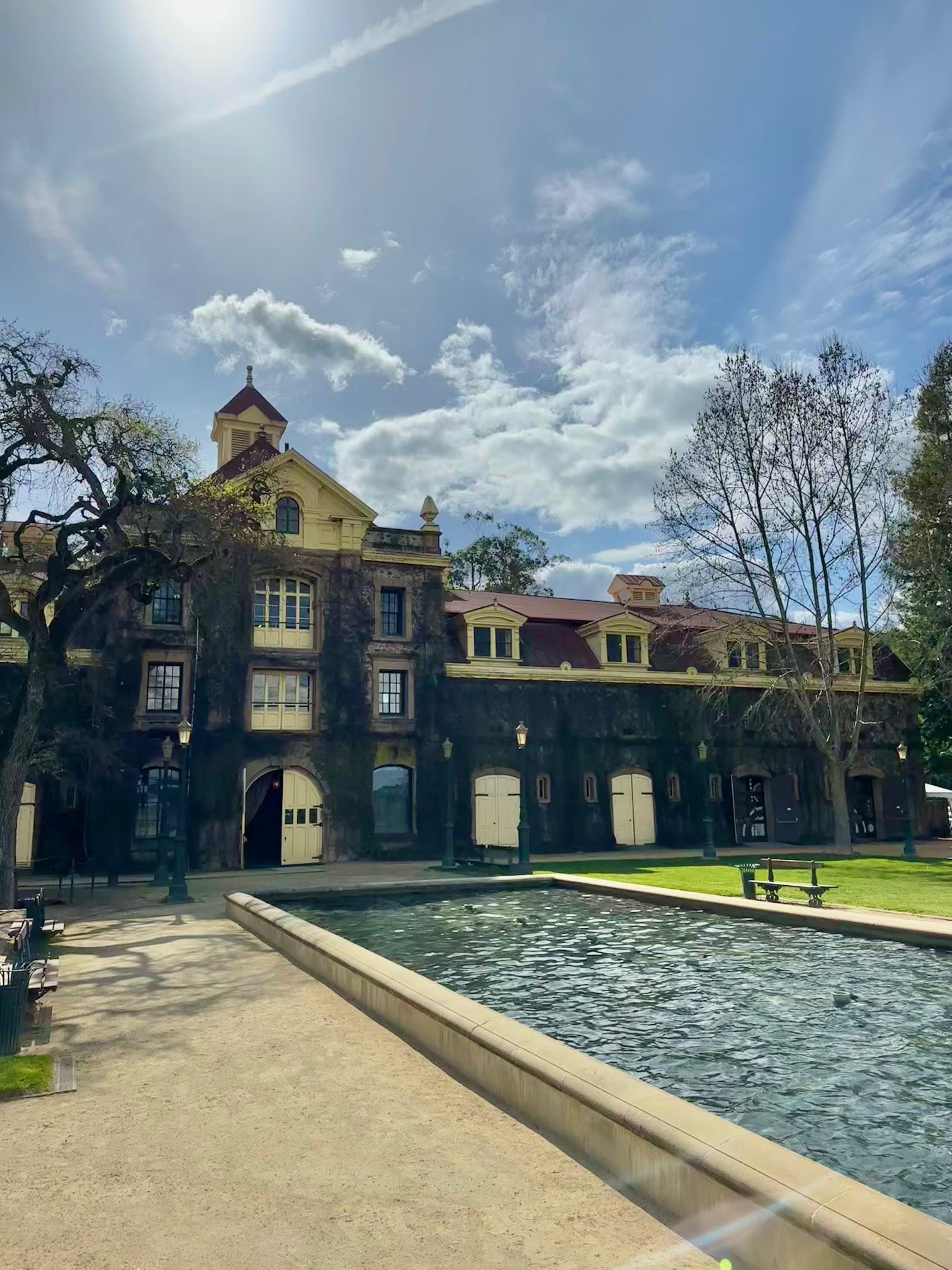 An historic building surrounded by trees stands tall against a clear sky dotted with clouds.