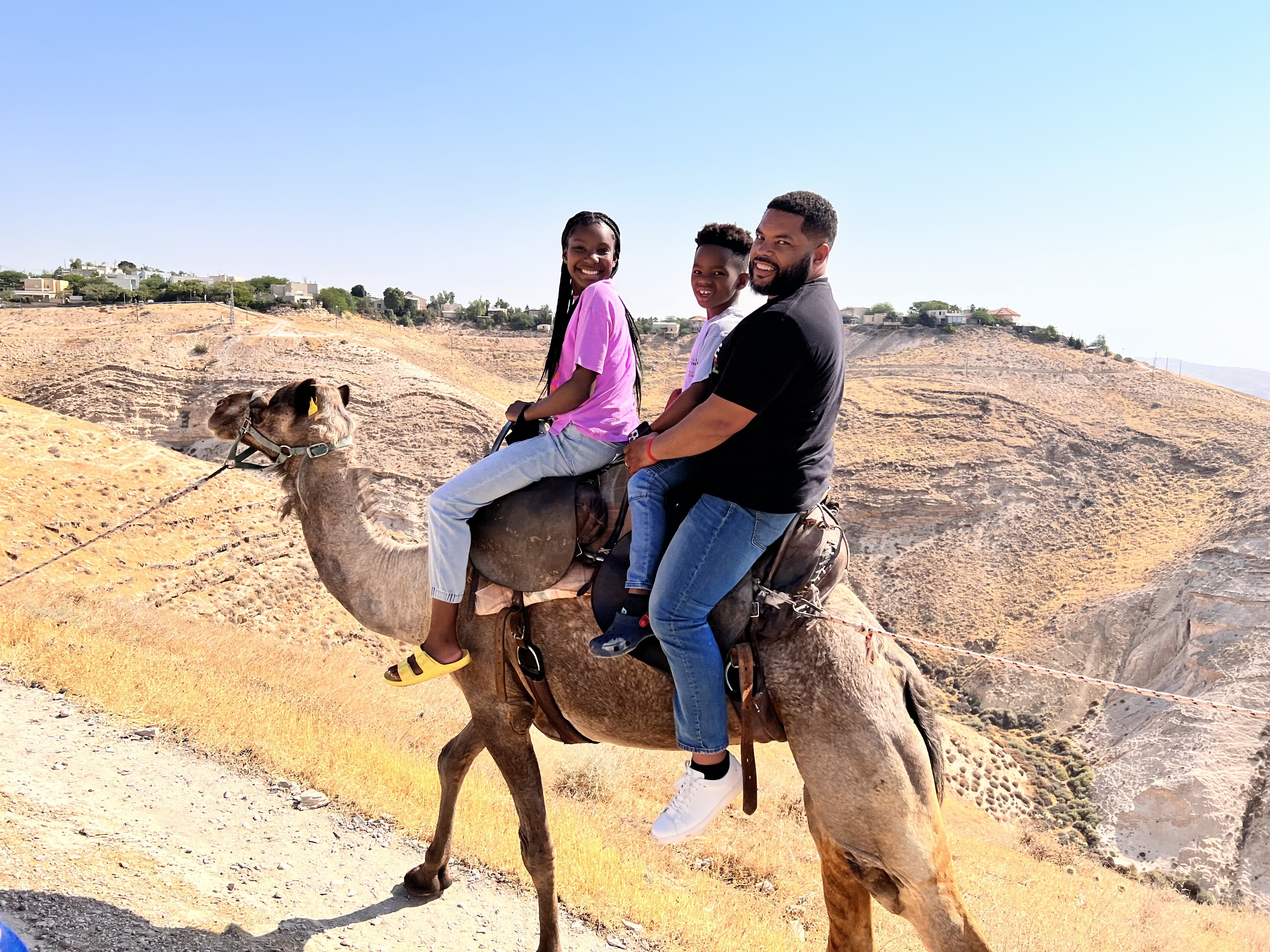 a man rides a camel in the desert with his two kids