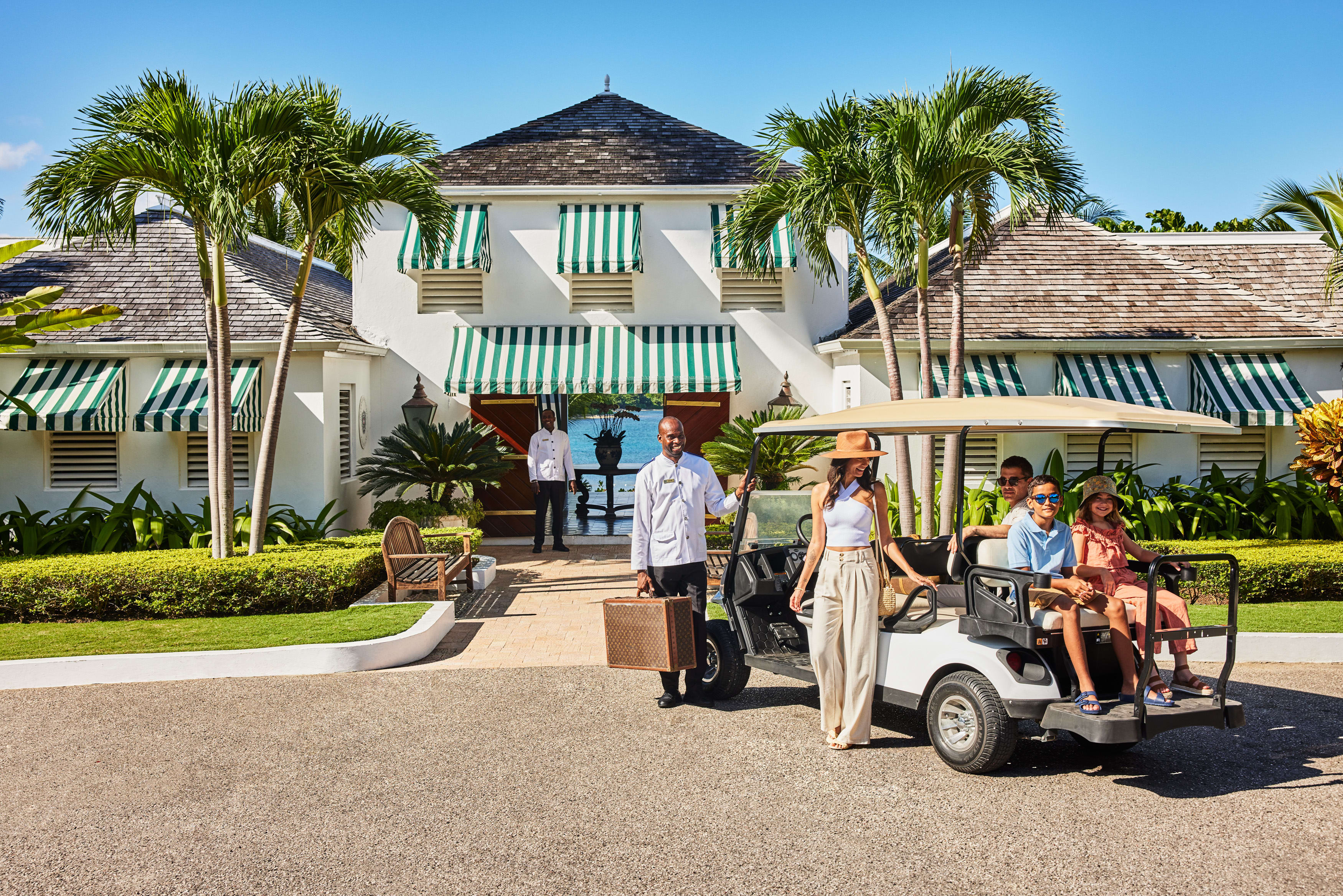 A family getting into a golf cart outside a hotel building with green and white shutters