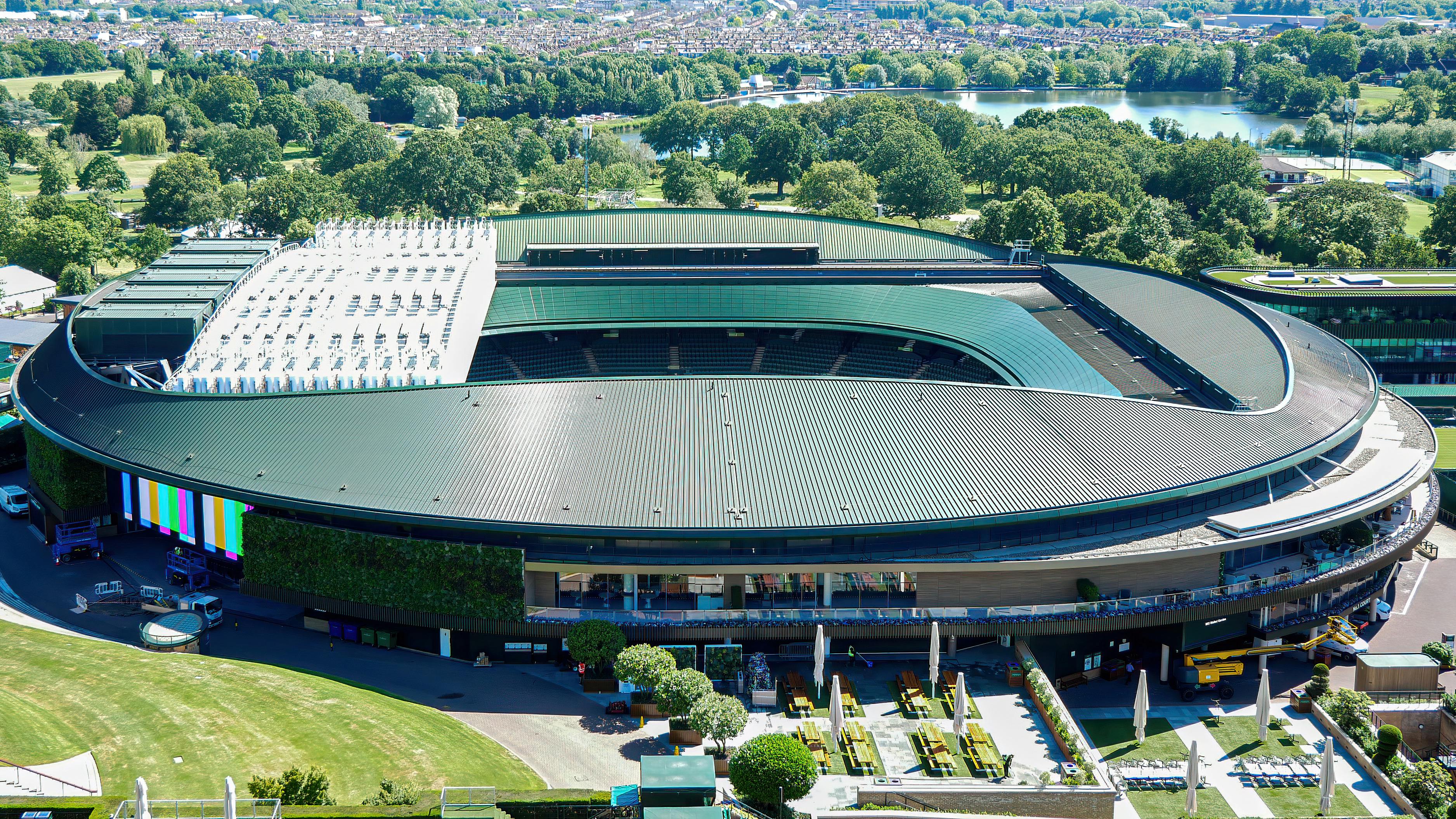 A view from above of a large green-colored tennis stadium surrounded by trees and fields.