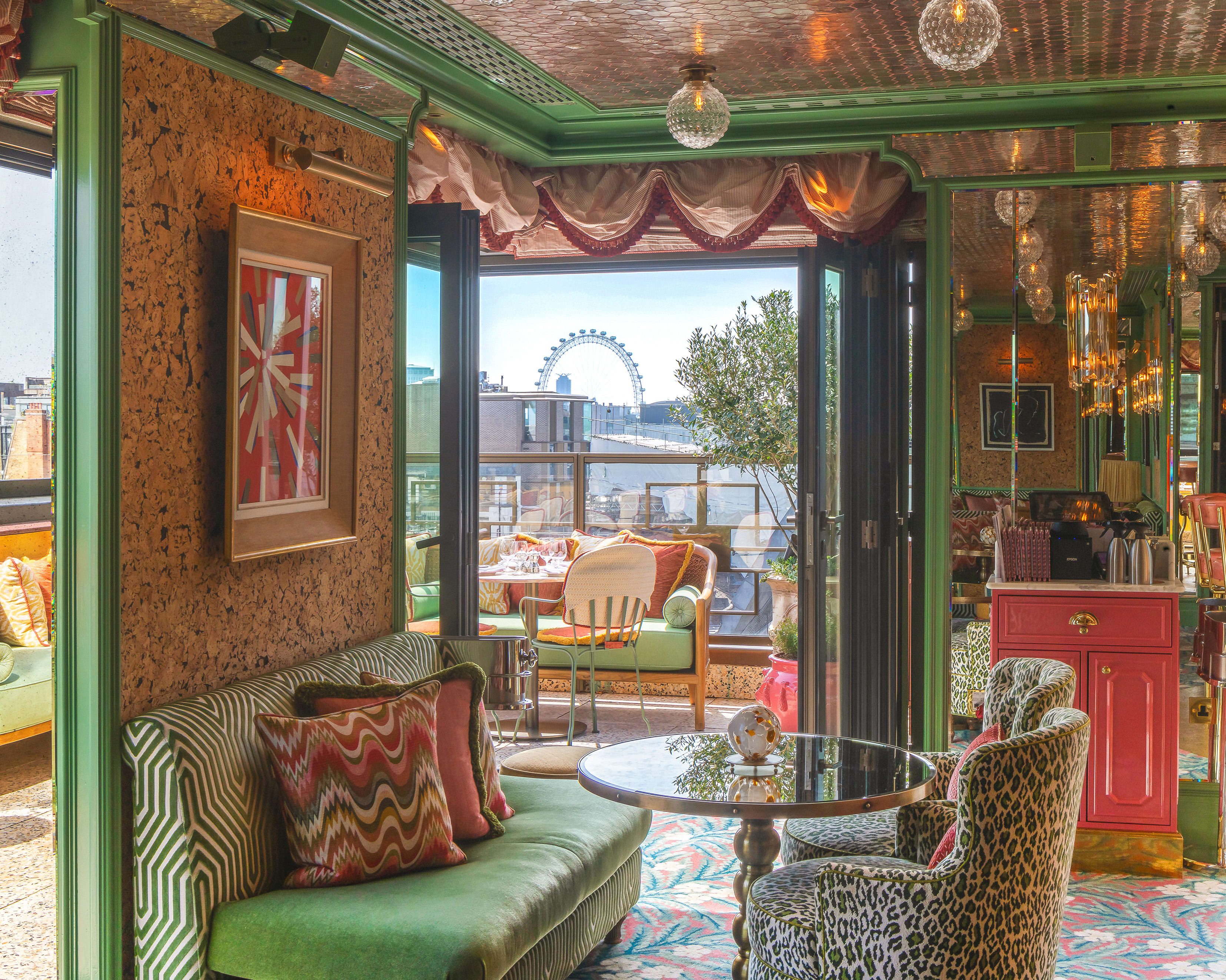 A colorful dining area with gree furnishings and fixtures with a terrace showing London city views.