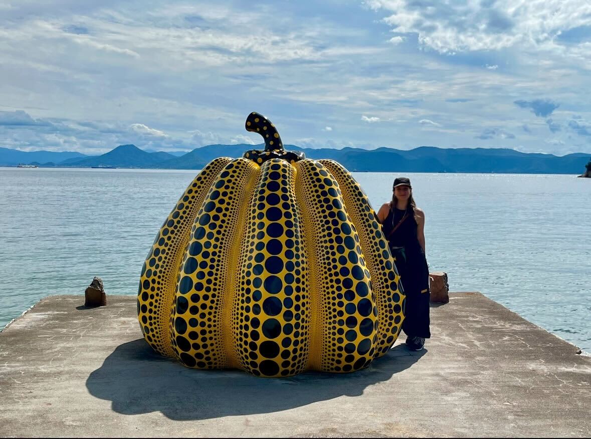 a woman stands next to a large sculptural pumpkin