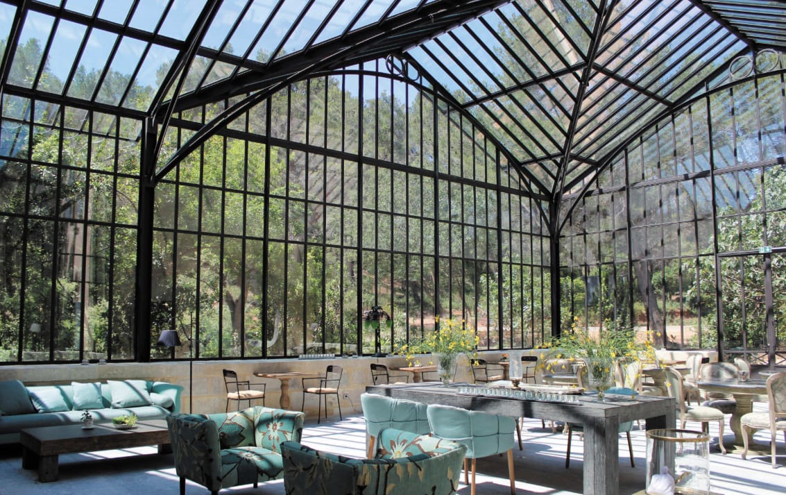 A dining area in a tall iron glass structure with views of trees