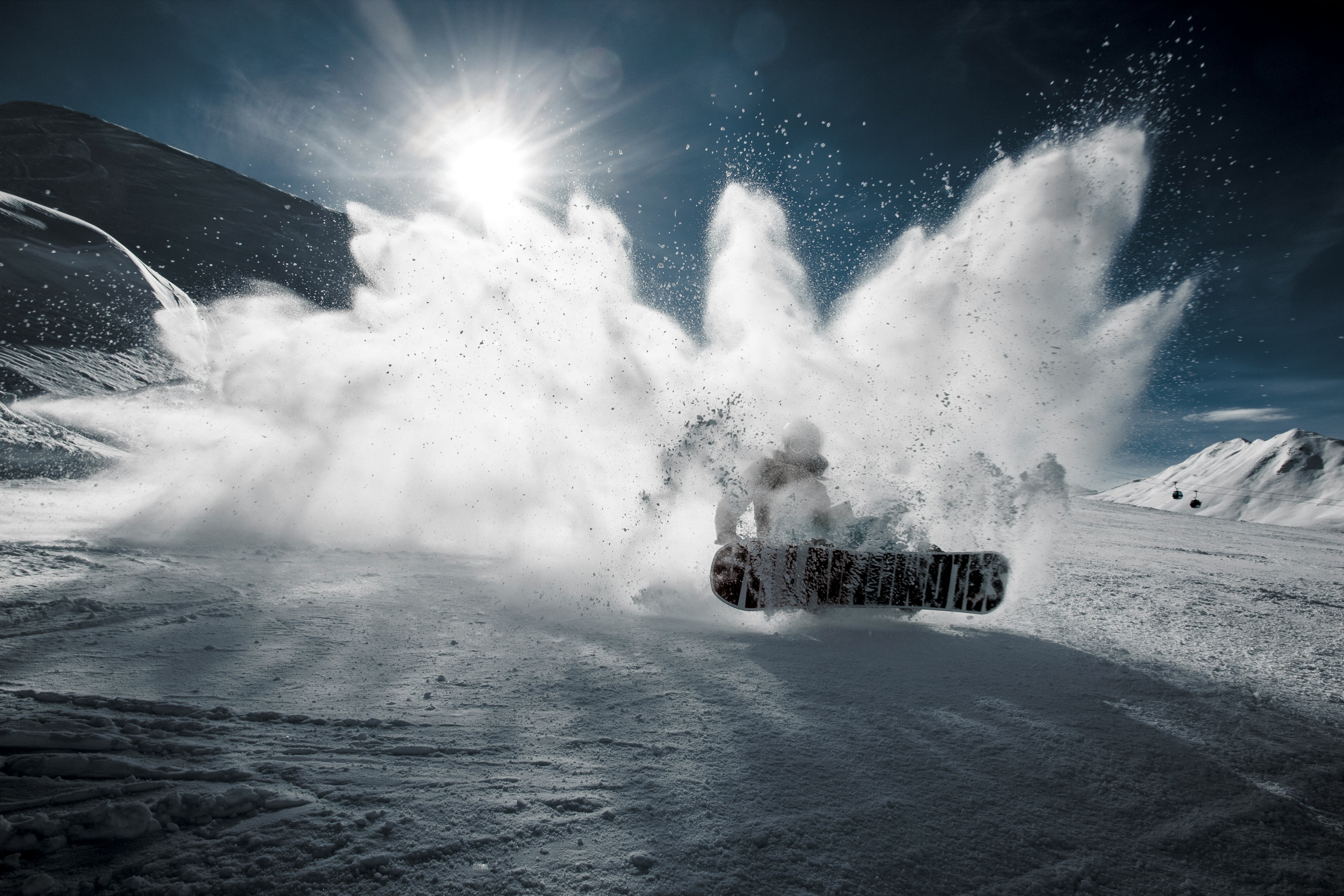 Snow being kicked up at the camera from a snowboarder with the sun shining above