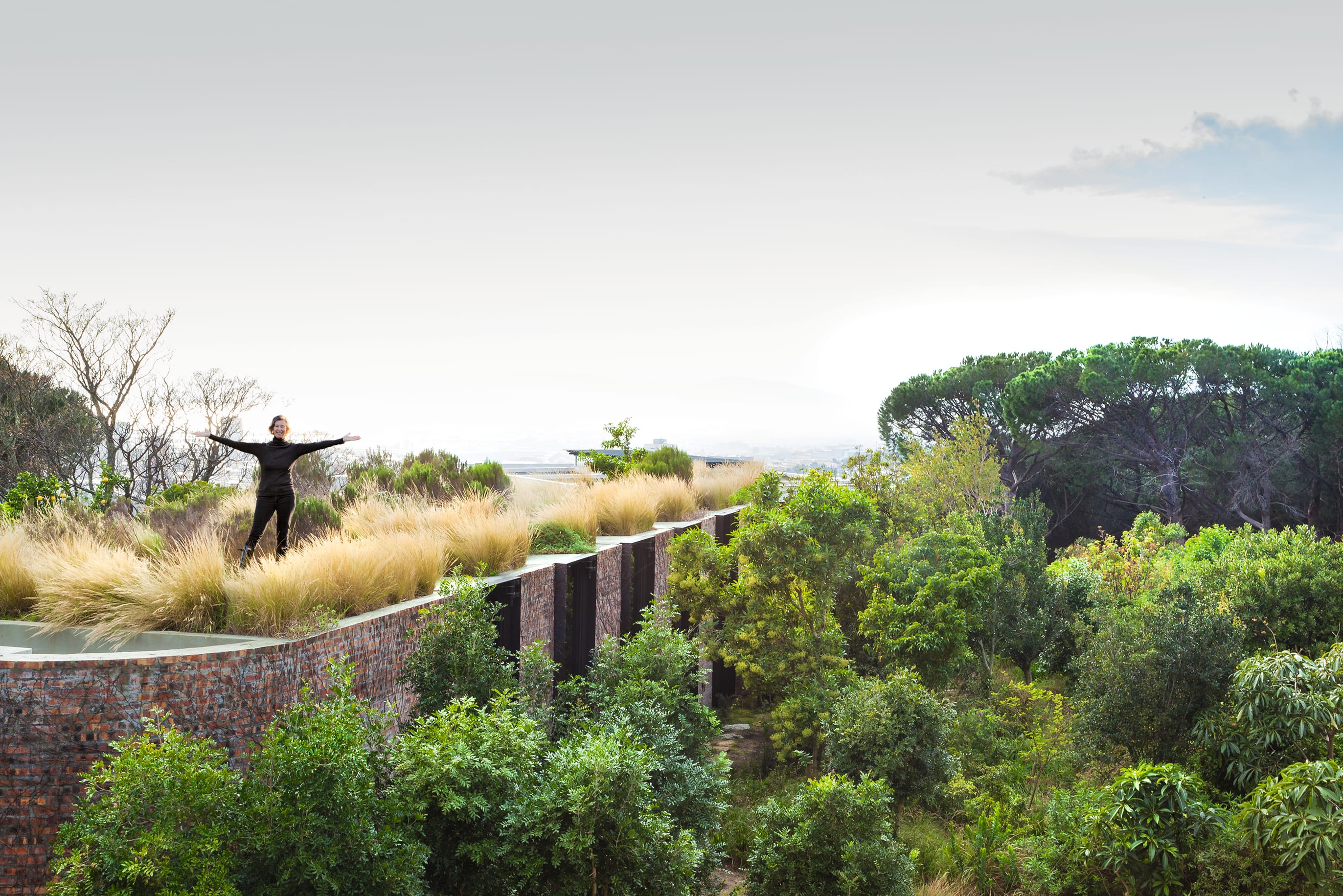 a woman stands on a stone wall in a lush garden