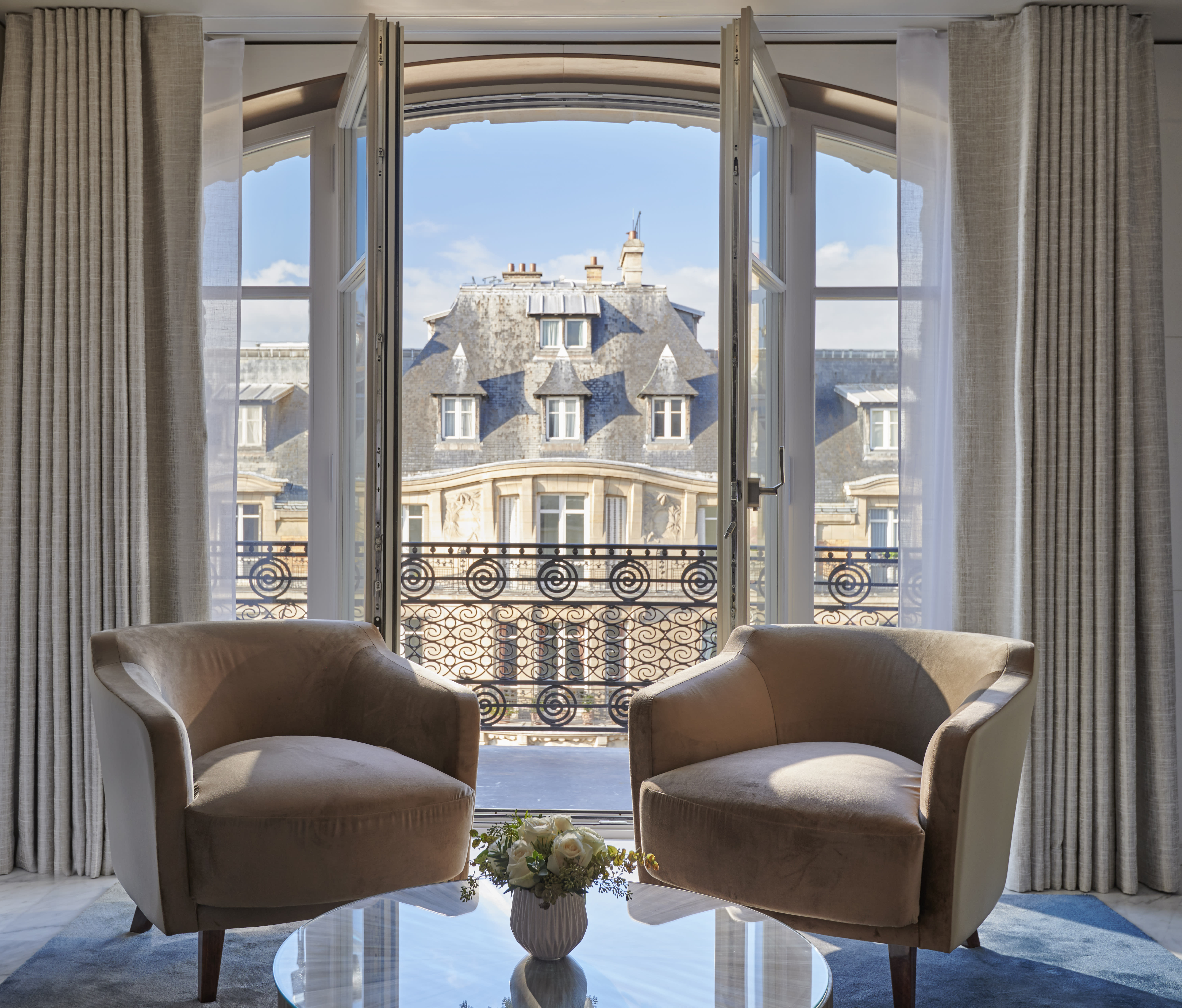 two plush chairs near an open window overlooking Paris