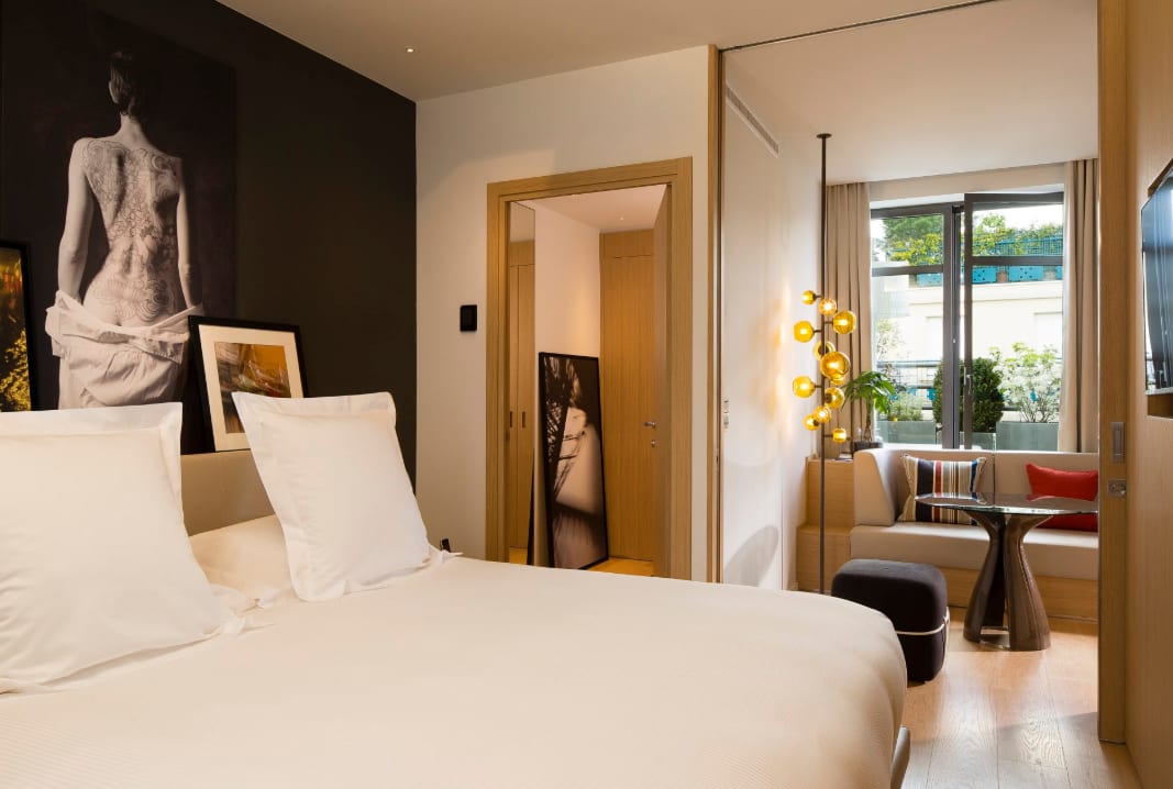 A contemporary hotel room with natural woods tones, white bedding and a small seating area.