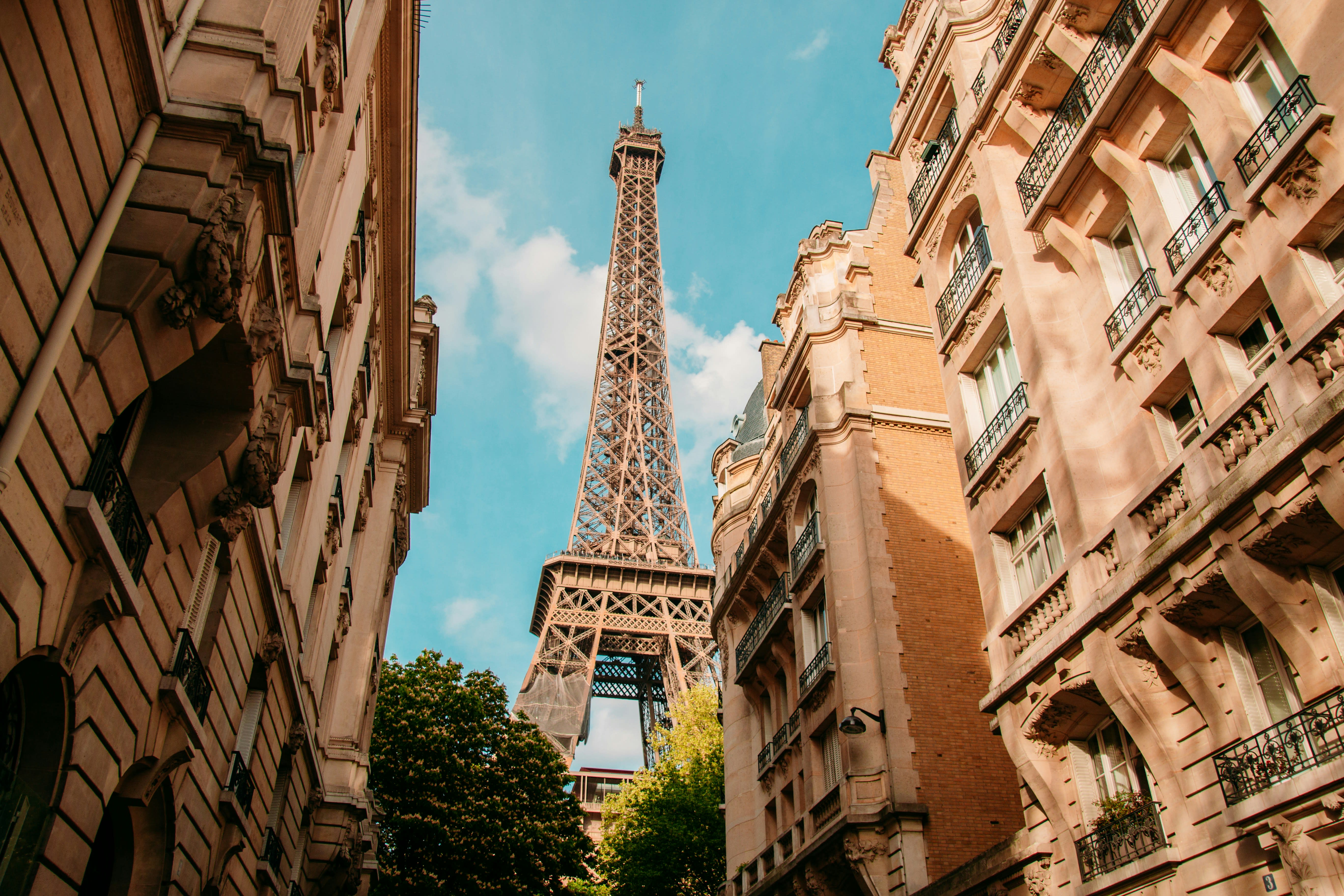 A view from below of the Eiffel Tower in between typical Parisian buildings on a sunny day.