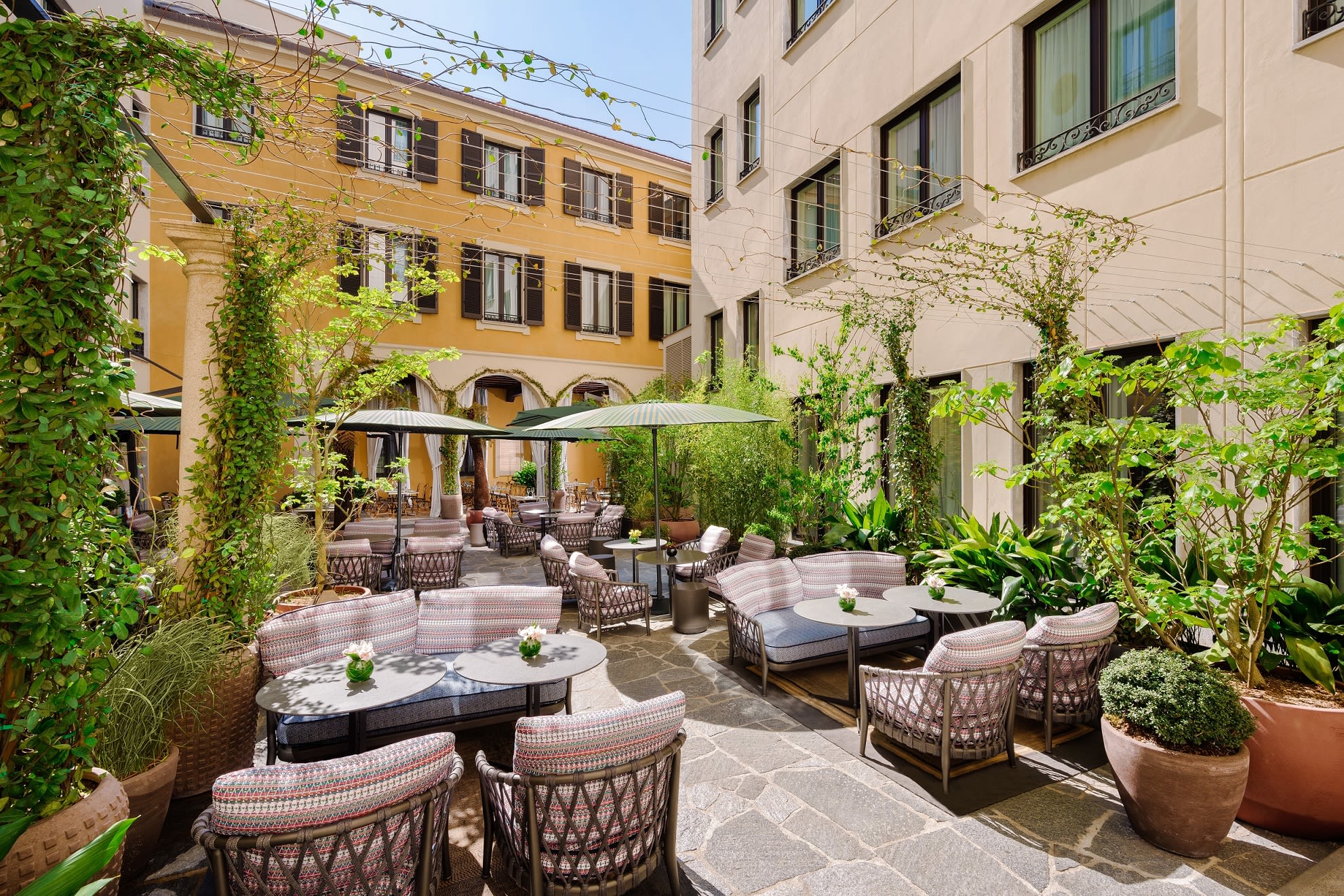 A hotel courtyard setting with lounge seating, umbrellas and greenery