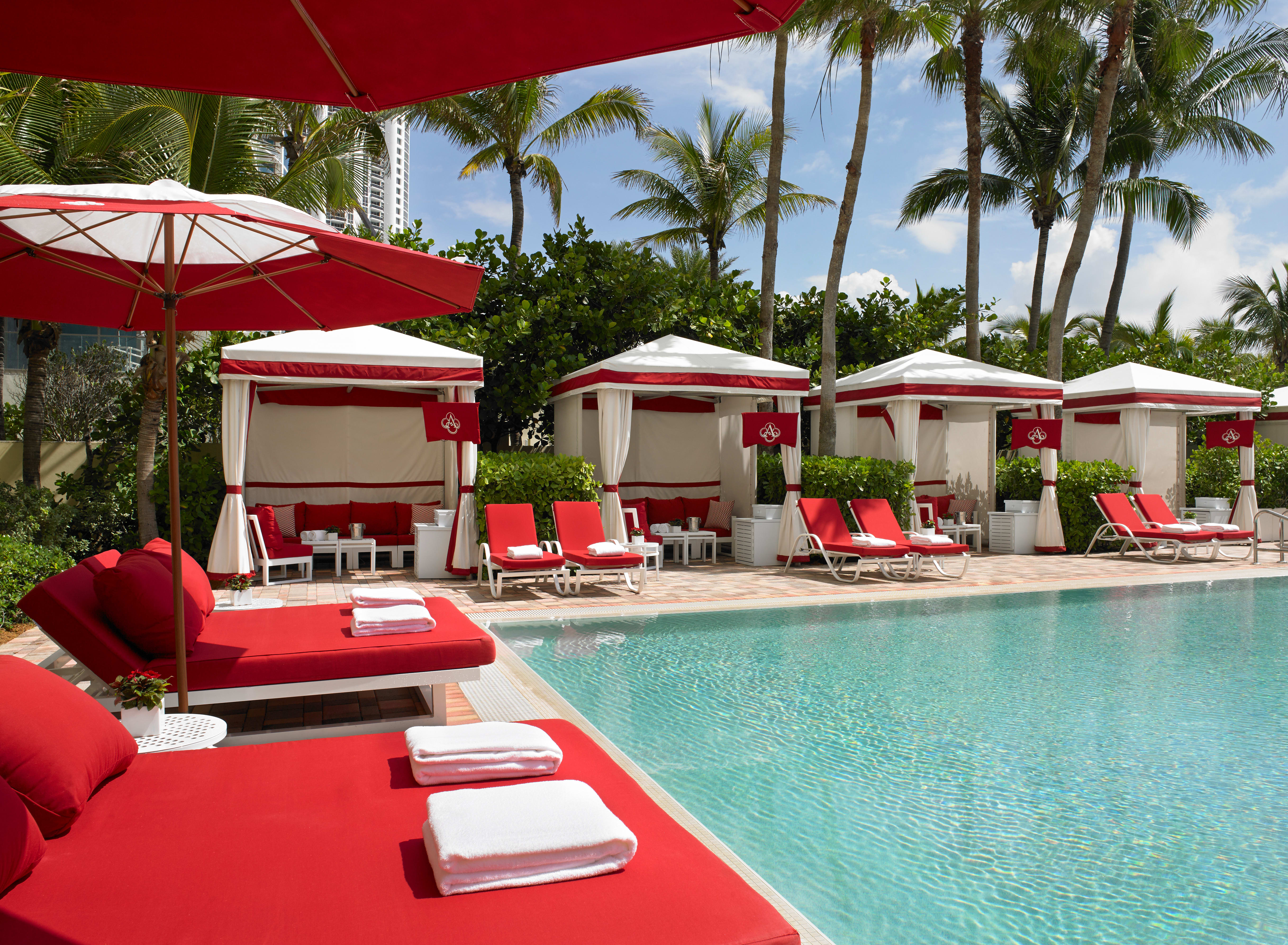 A hotel pool area with bright red loungers and umbrellas
