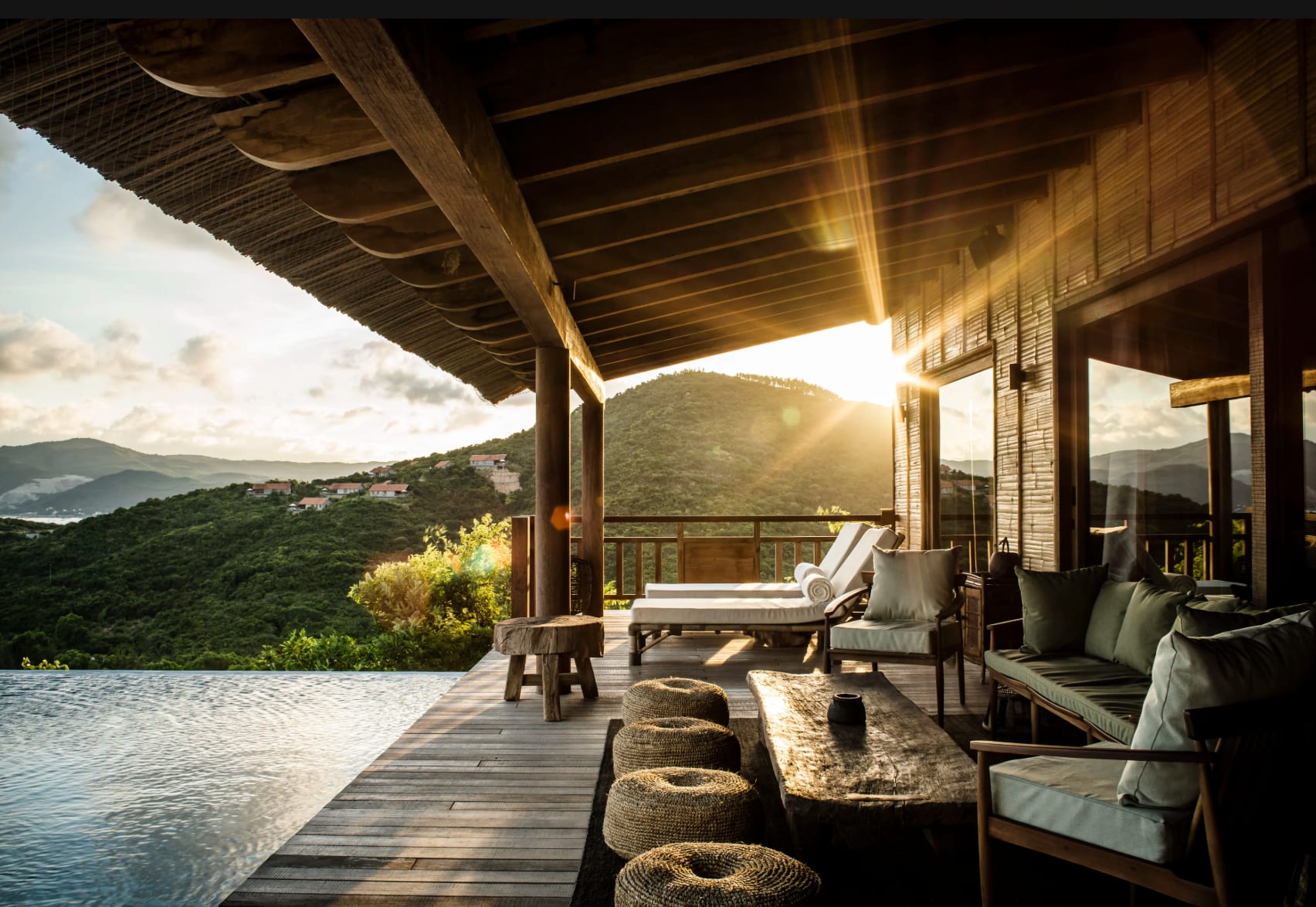 A hotel deck with pool and loungers overlooking lush mountains