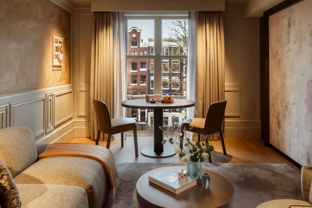 An elegant hotel living room with table, charis and lounge area and views of typical buildings in Amsterdam