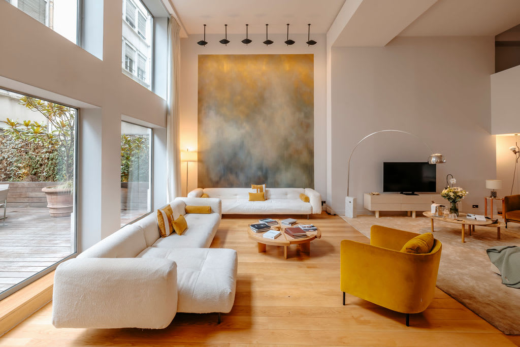A contemporary living space with low cream sofas, high ceilings and a mustard armchair