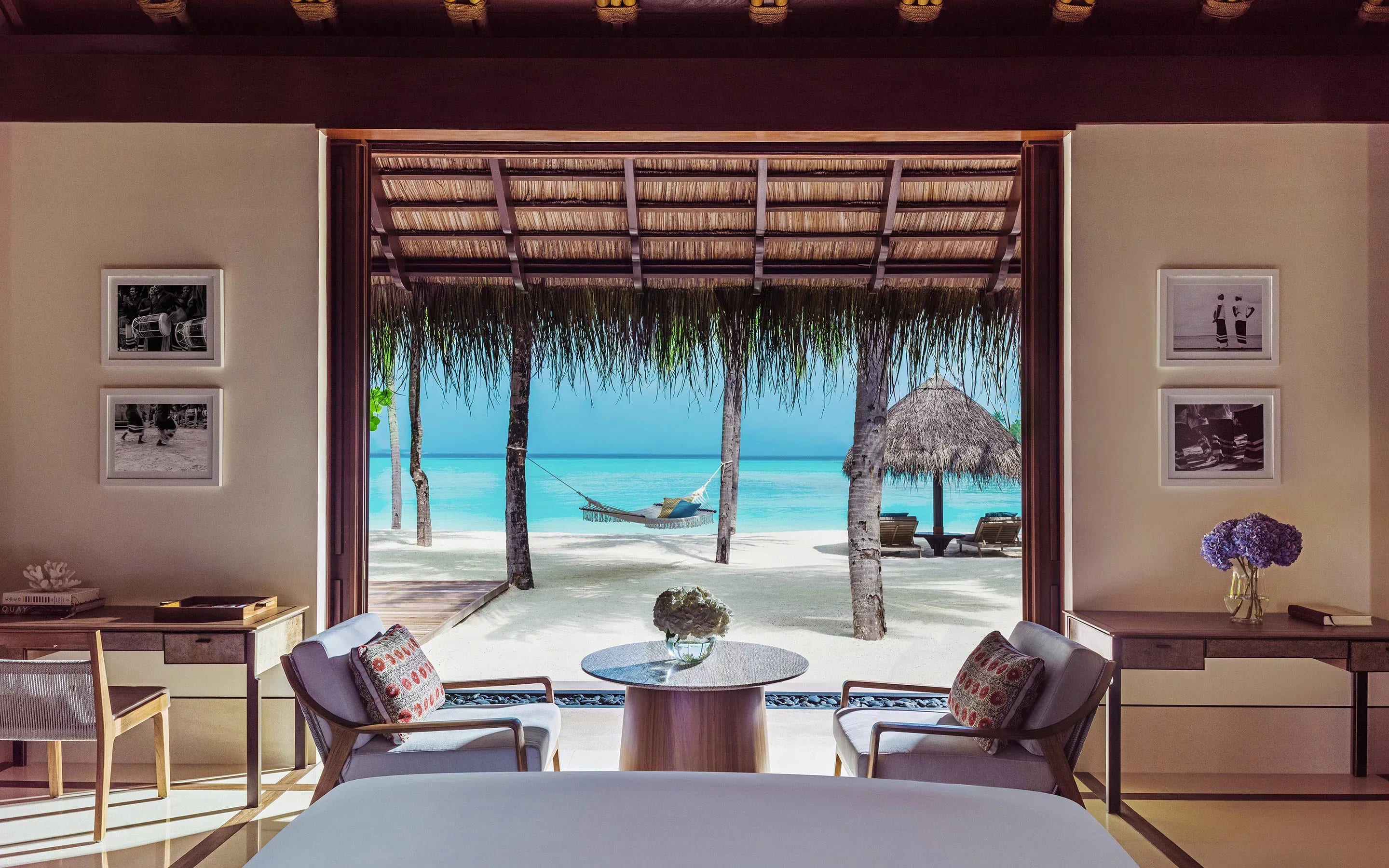 beach bungalow looking out at a hammock between palm trees and the turquoise sea beyond