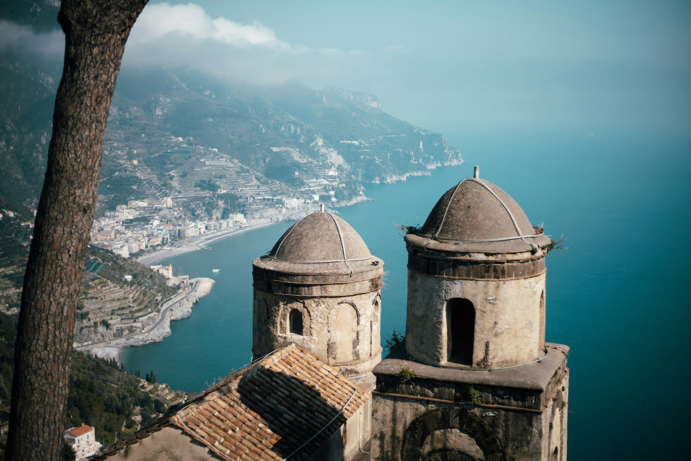 View of ancient domed towers high above hillside villages and blue ocean water during day