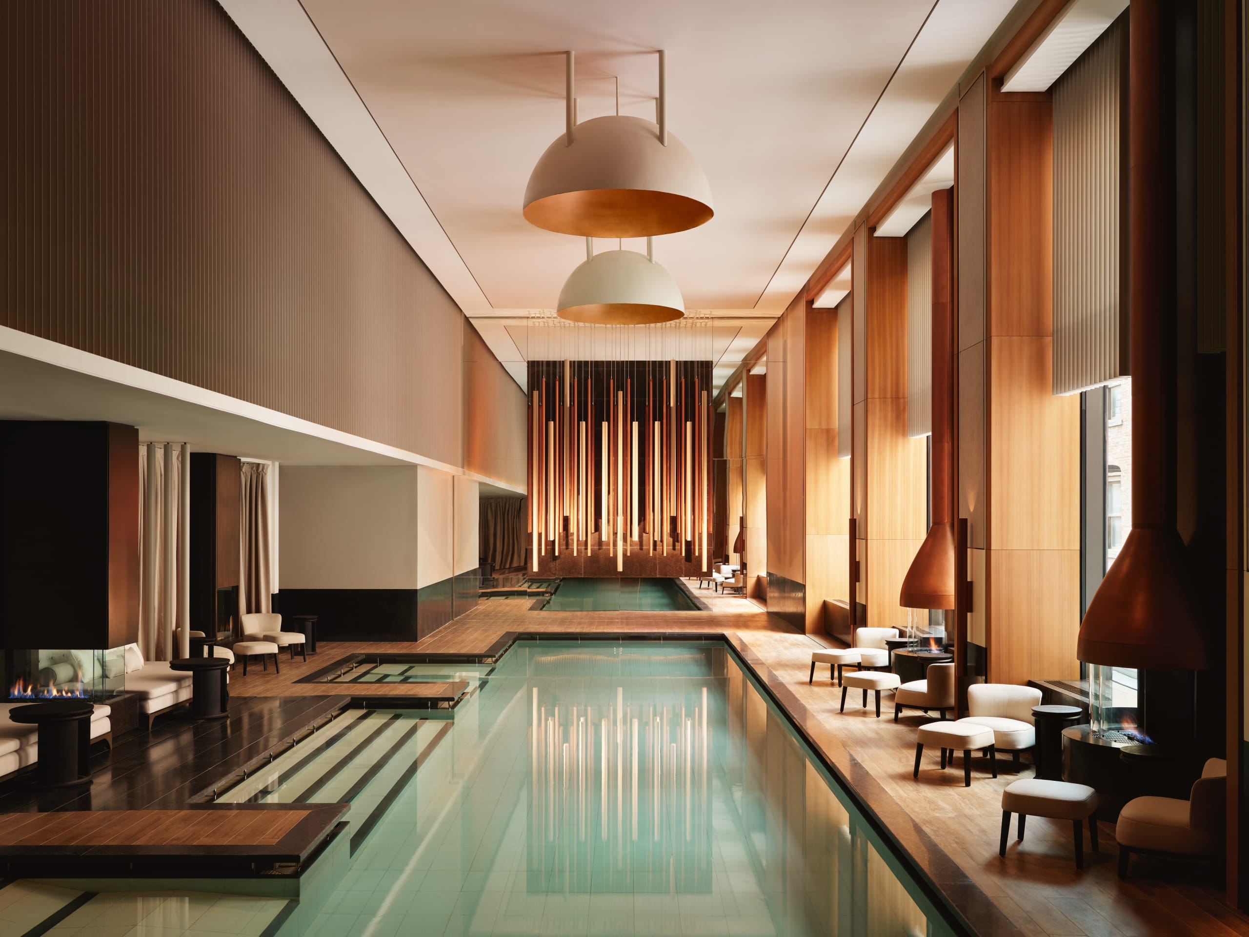 An indoor hotel pool with high ceiling, hanging lights and floor-to-ceiling windows