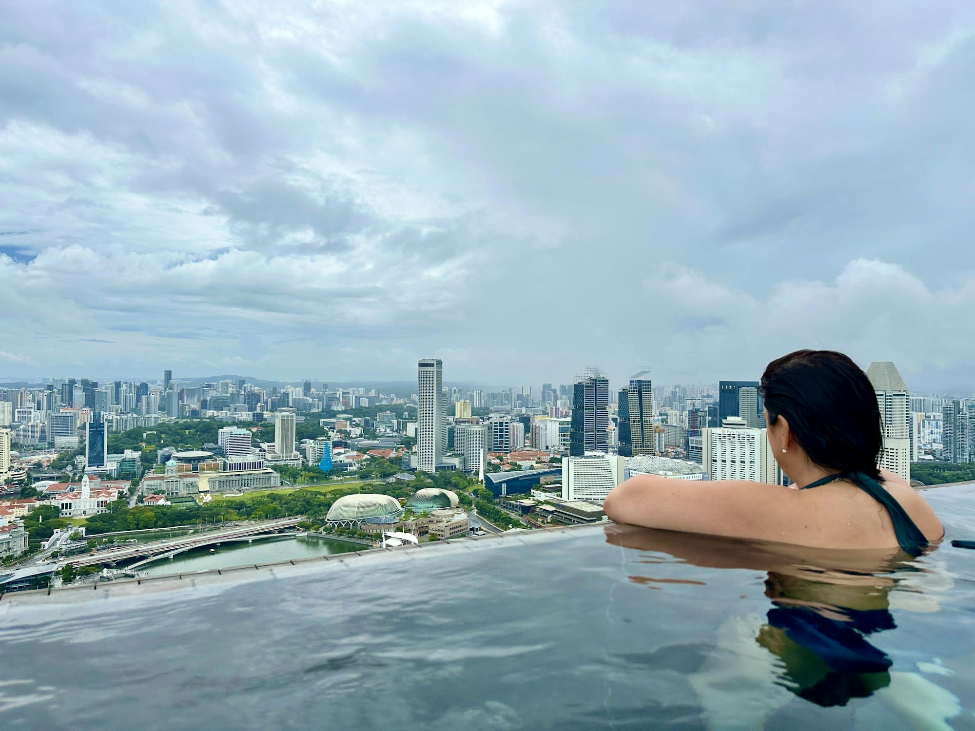 a woman sits in an infinity-edged pool overlooking a city