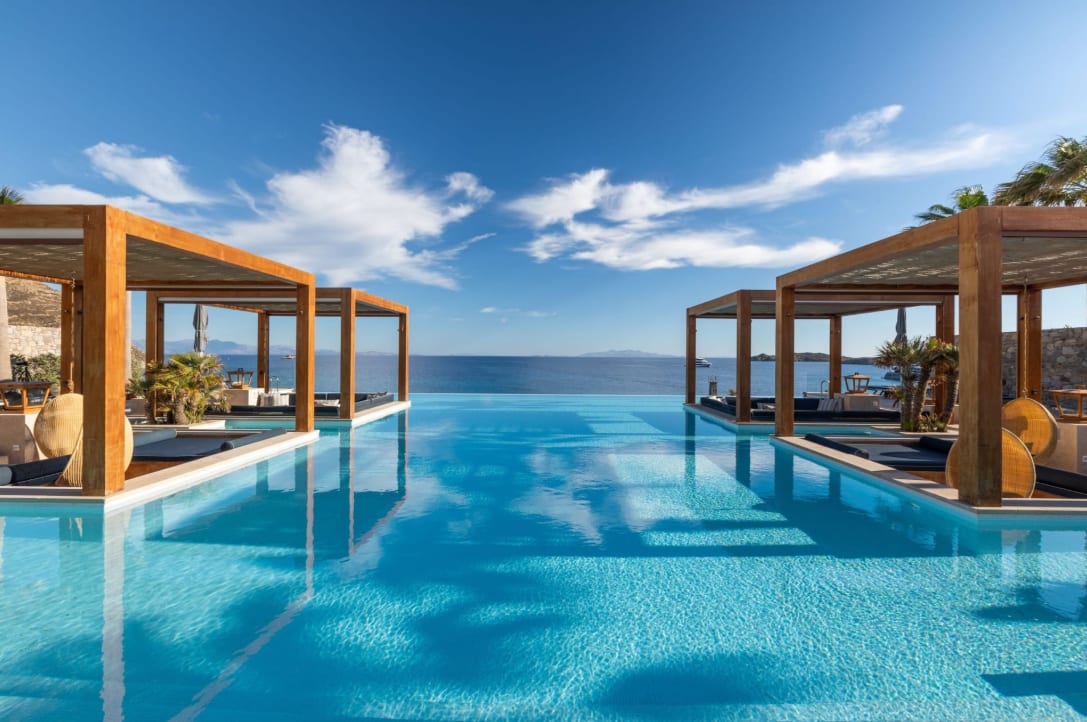 An infinity pool facing the ocean with brown cabana structures around it