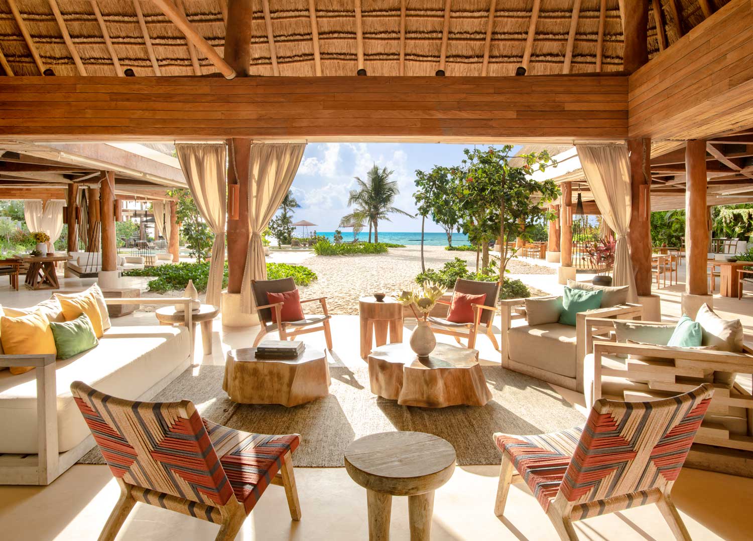 A hotel bar area by the beach with wooden roof and low seating.