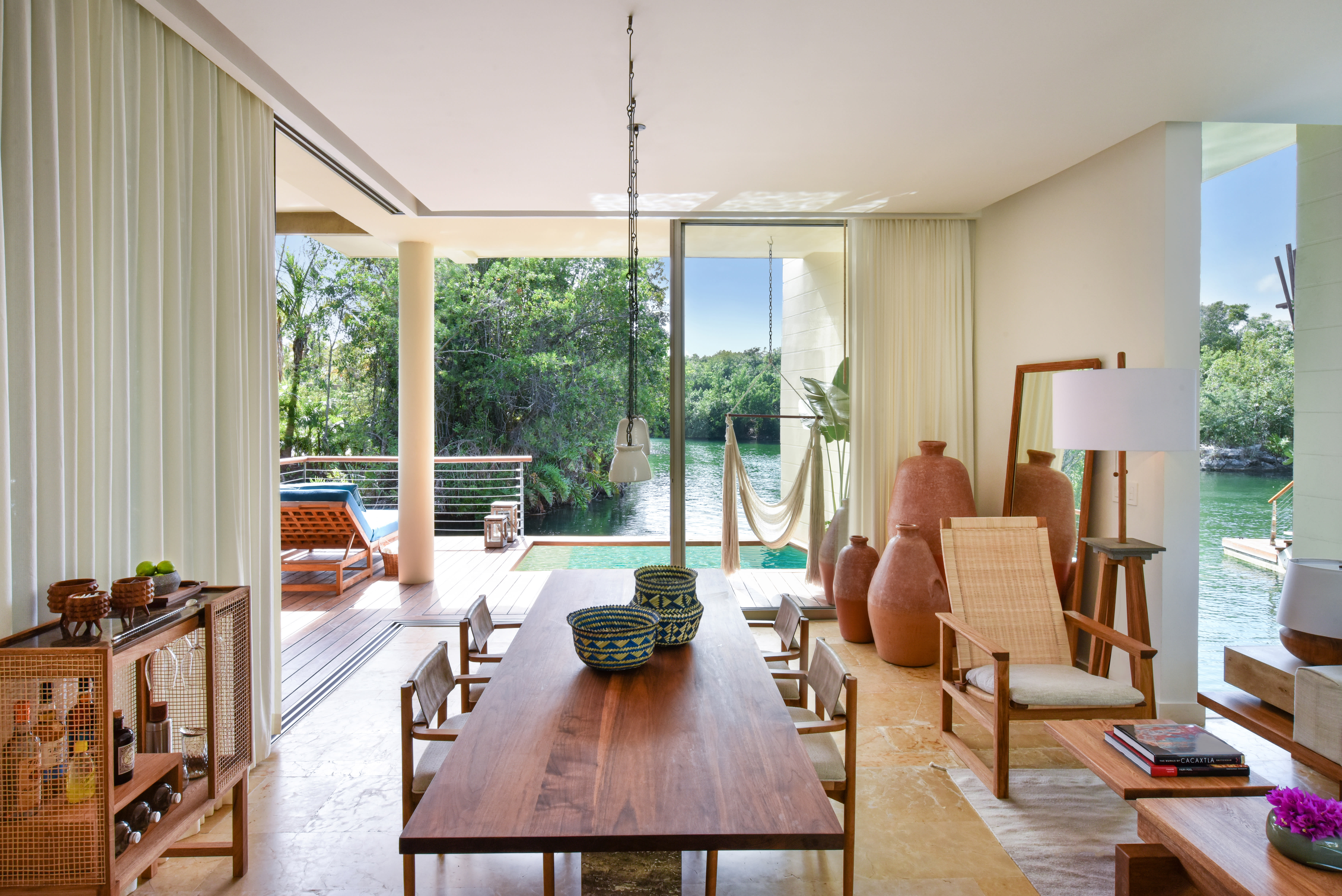 An elegant hotel suite with dining table and neutral decor looking out onto a private plunge pool and lagoon